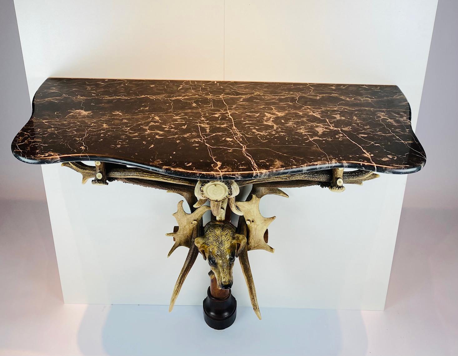 A  rara console in corna Black Forest del XIX secolo con piano in marmo.

Sotto la testa di un cane da caccia in terracotta con occhi di vetro. 
In cima un bellissimo marmo nero.