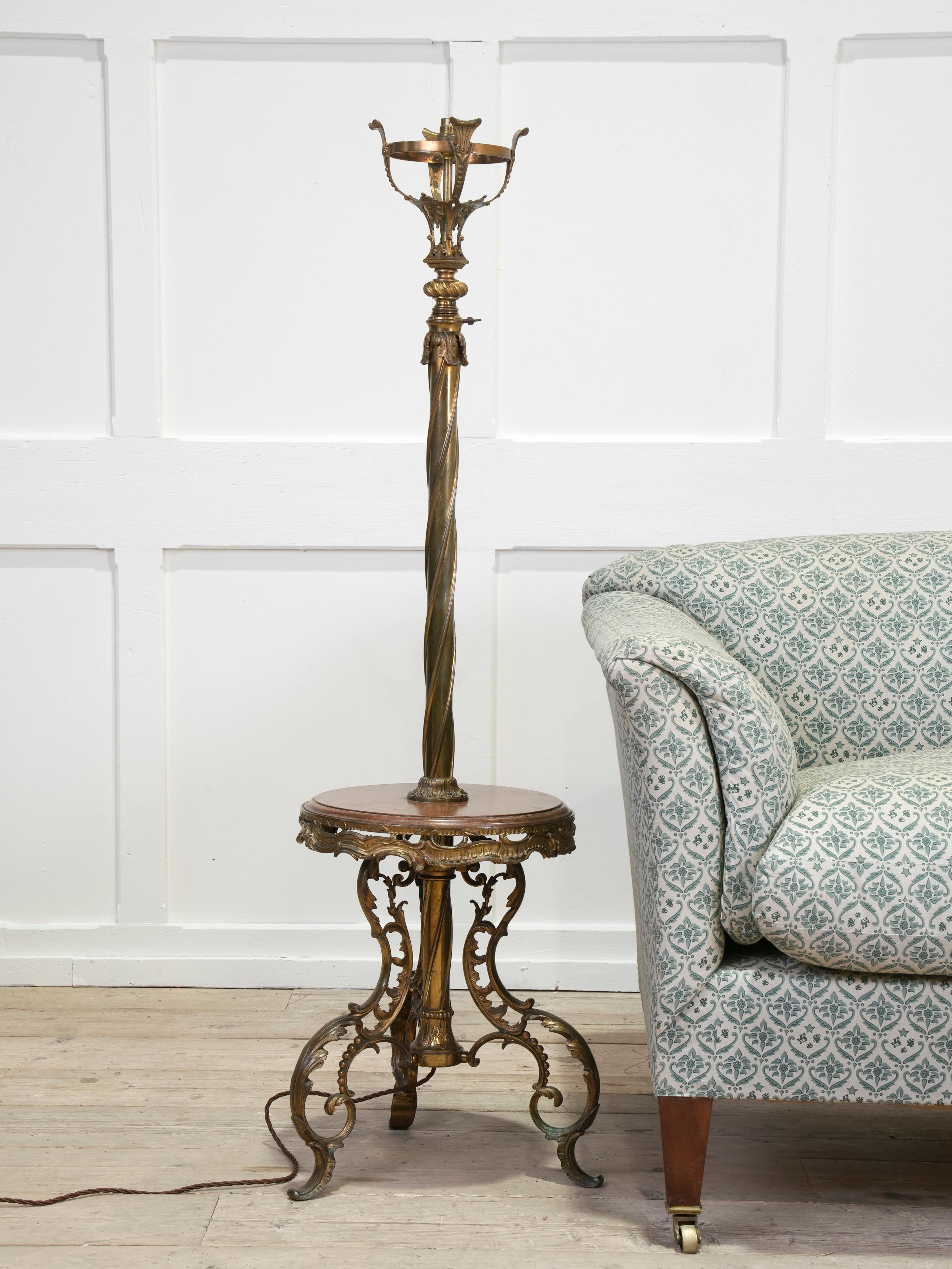 An outrageous gilt brass adjustable standard lamp with a low oak shelf, converted to electricity.