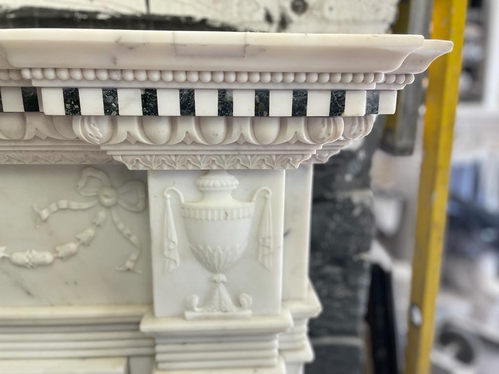 Cheminée du XIXe siècle en marbre de Carrare et Verde Antico
Dans le style George III
L'étagère inversée avec une corniche à denticules au-dessus d'une frise de guirlandes de clochettes nouées par un ruban et suspendues par un médaillon, avec une