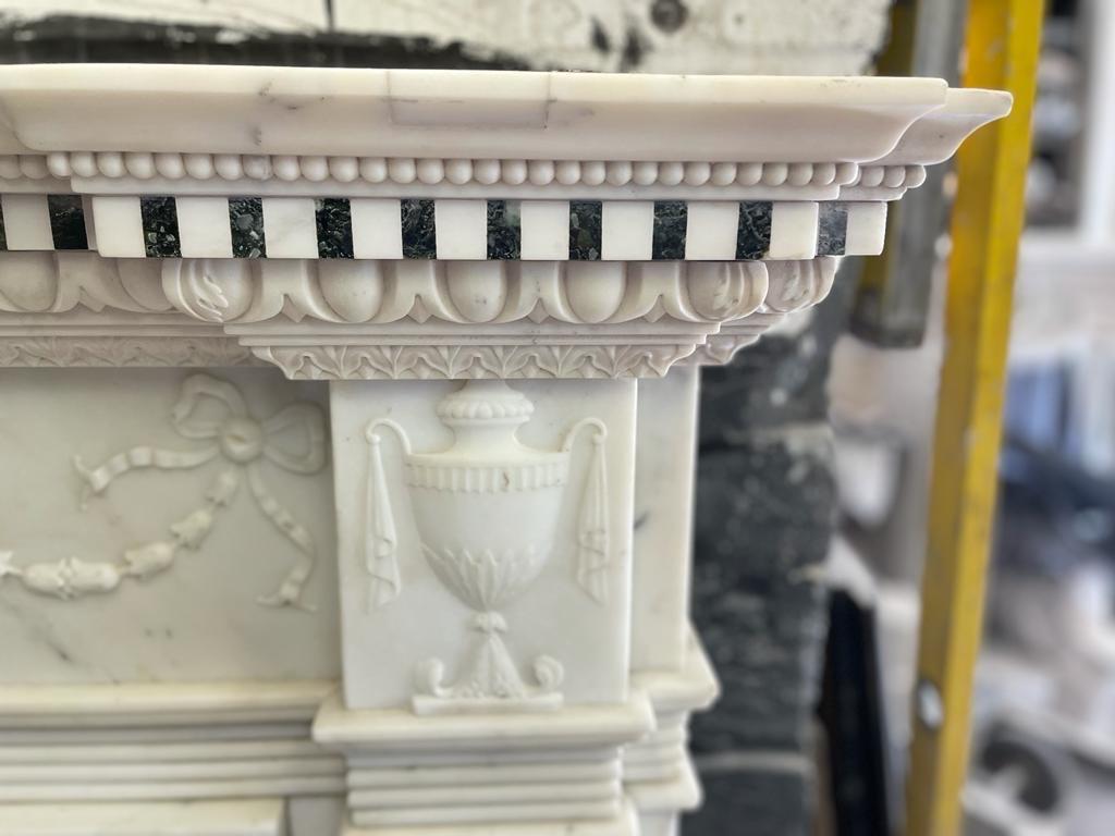 A 19th century Carrara and Verde Antico marble chimneypiece
In the George III style
The inverted breakfront shelf with dentil cornice above a ribbon tied and medallion hung bell husk garlanded frieze with central tablet carved with a draped