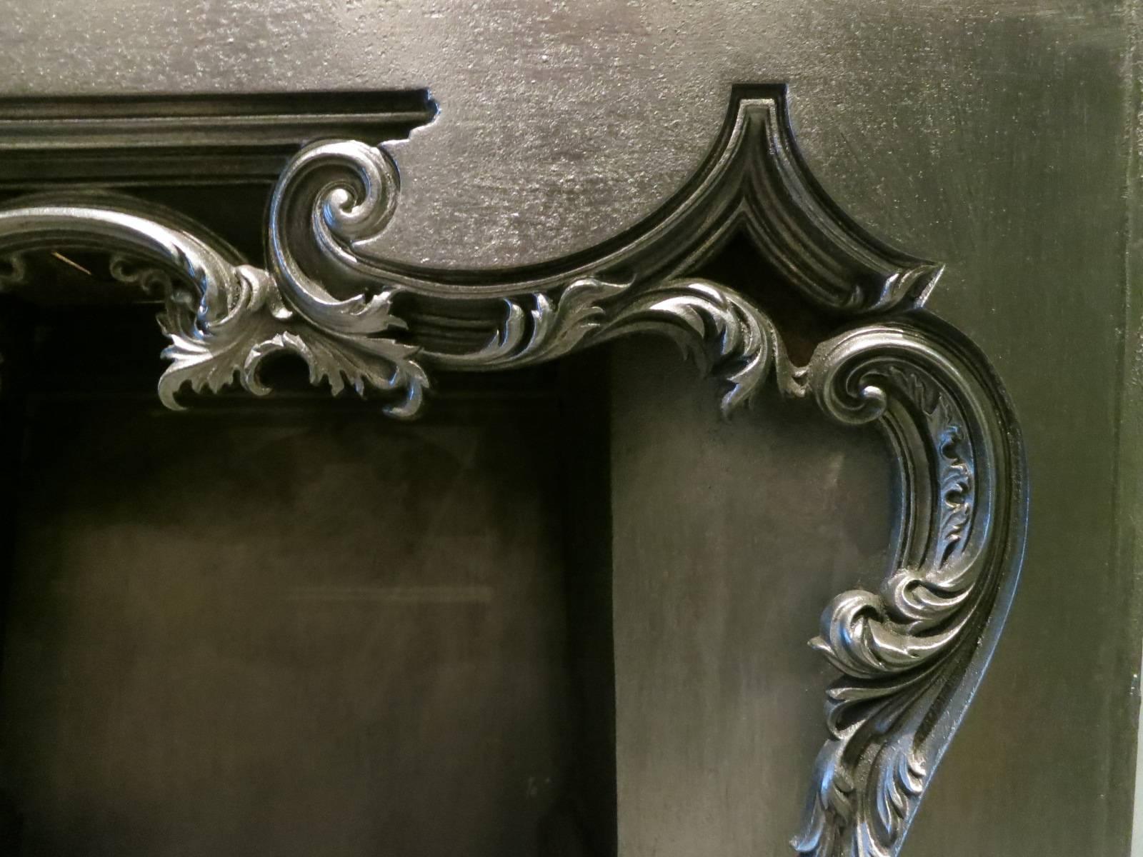 A large fireplace insert with decorative foliage castings framing the burning area, with plain inverted interior panels and back panel. The bowed front bars removable bars with conforming casting.