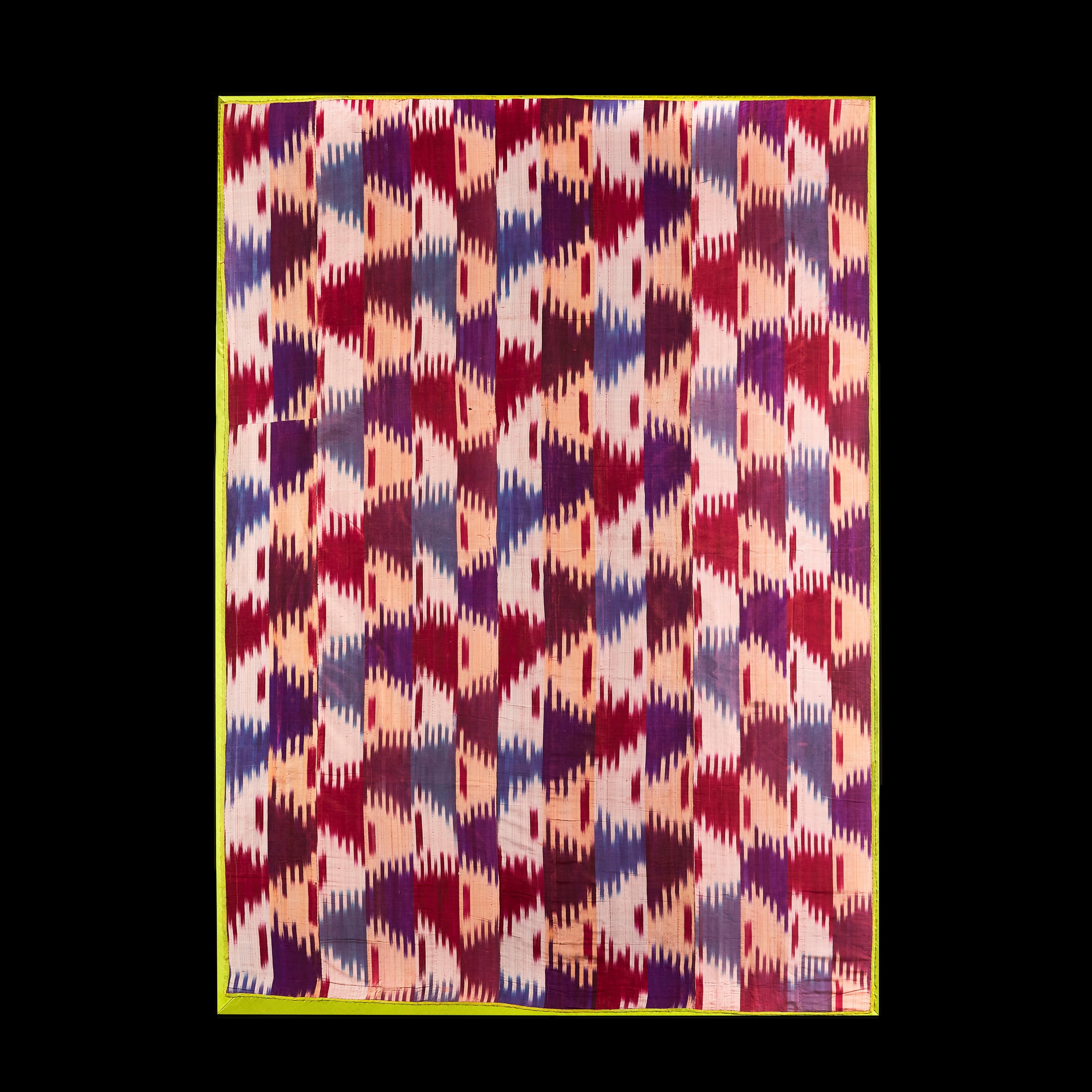 A large panel of Central Asian Ikat, decorated with diffuse colours in red, aubergine, and pale cream, in a continuous abstract pattern, bordered with lime green silk, stretched and now mounted, lined to the back.