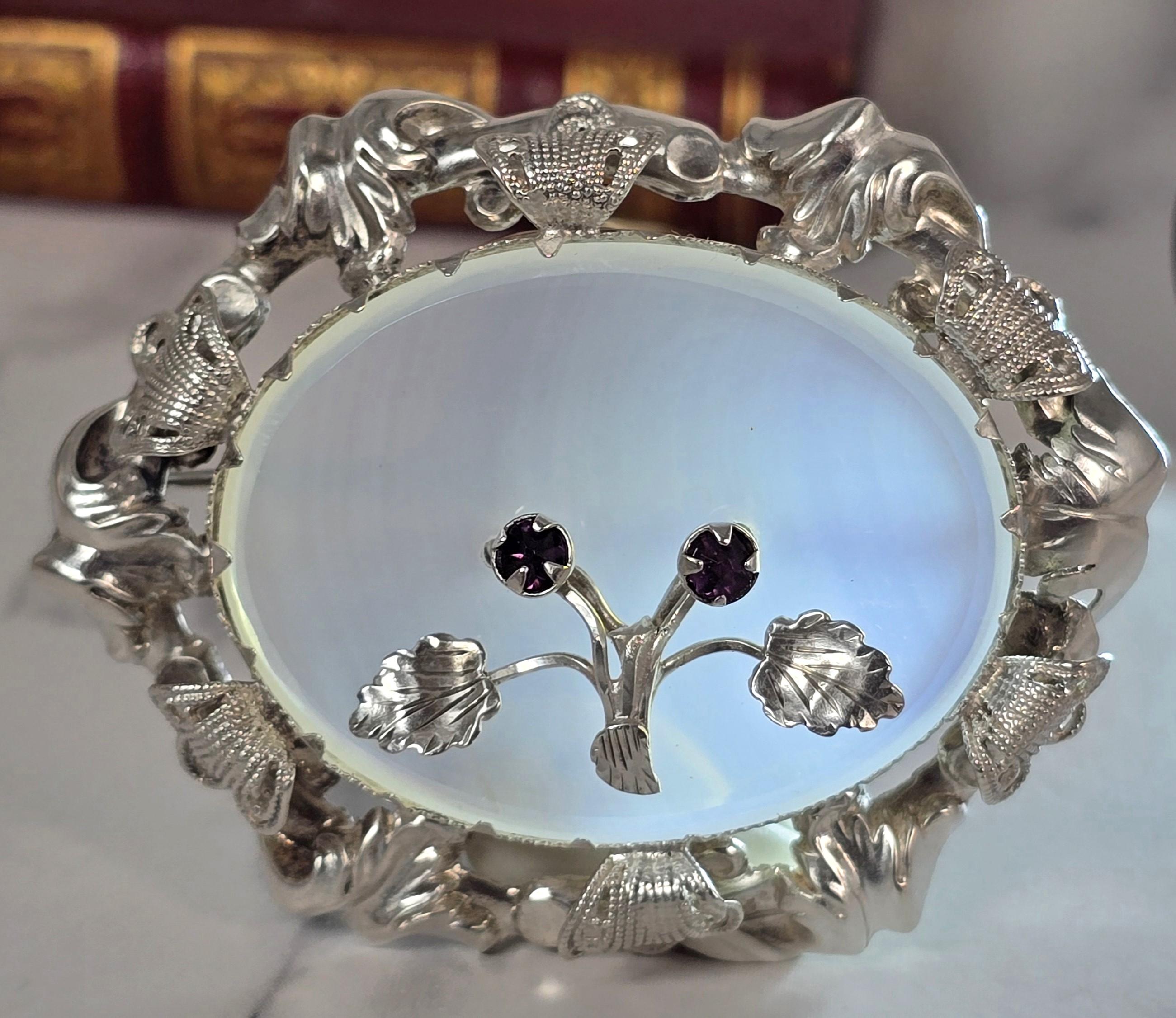 This stunning piece of Victorian handmade jewellery is made from unmarked but tested silver, which forms an oval foliate wreath shaped mount with filigree detailing.

The mount has central claws which hold the oval opaque white polished chalcedony