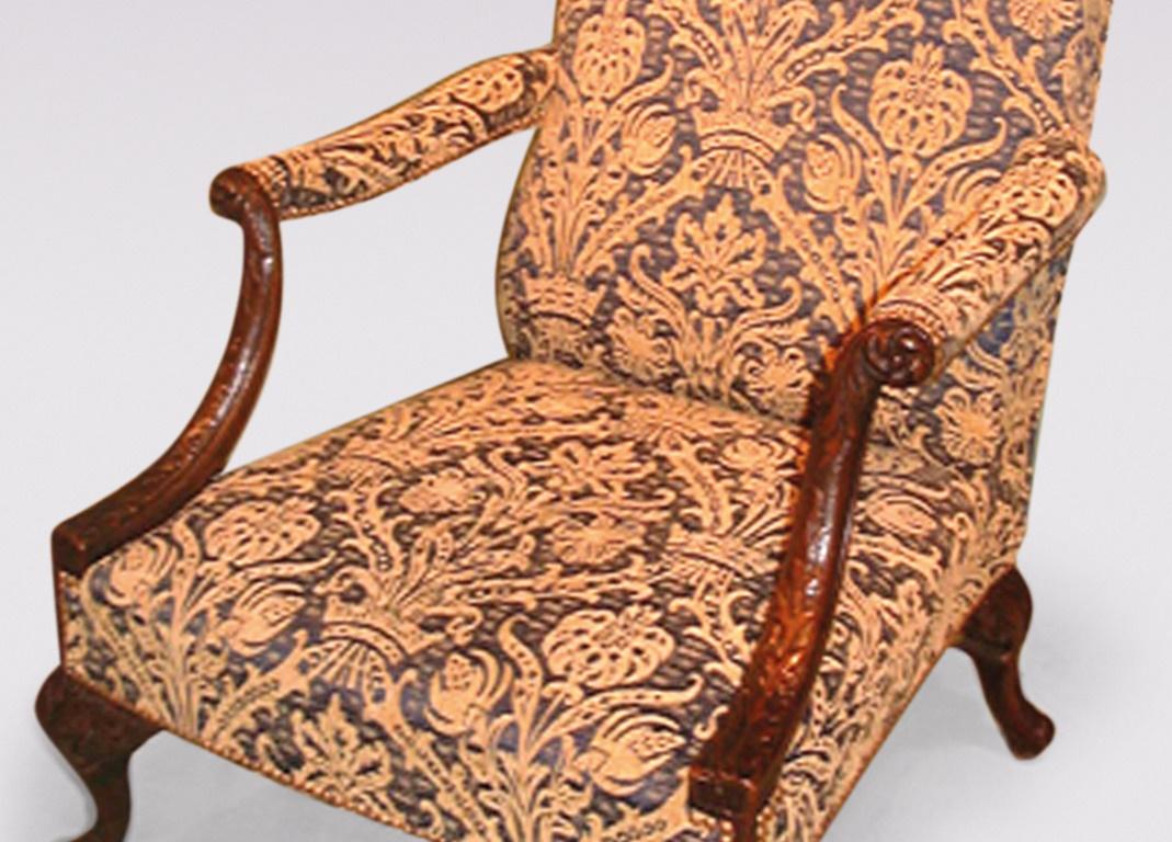 A mid-19th century Chippendale style mahogany Gainsborough chair having serpentine-topped upholstered back and floral carved set-back arms above stuffover seat supported on acanthus leaf and 'C' scroll carved cabriole legs.
