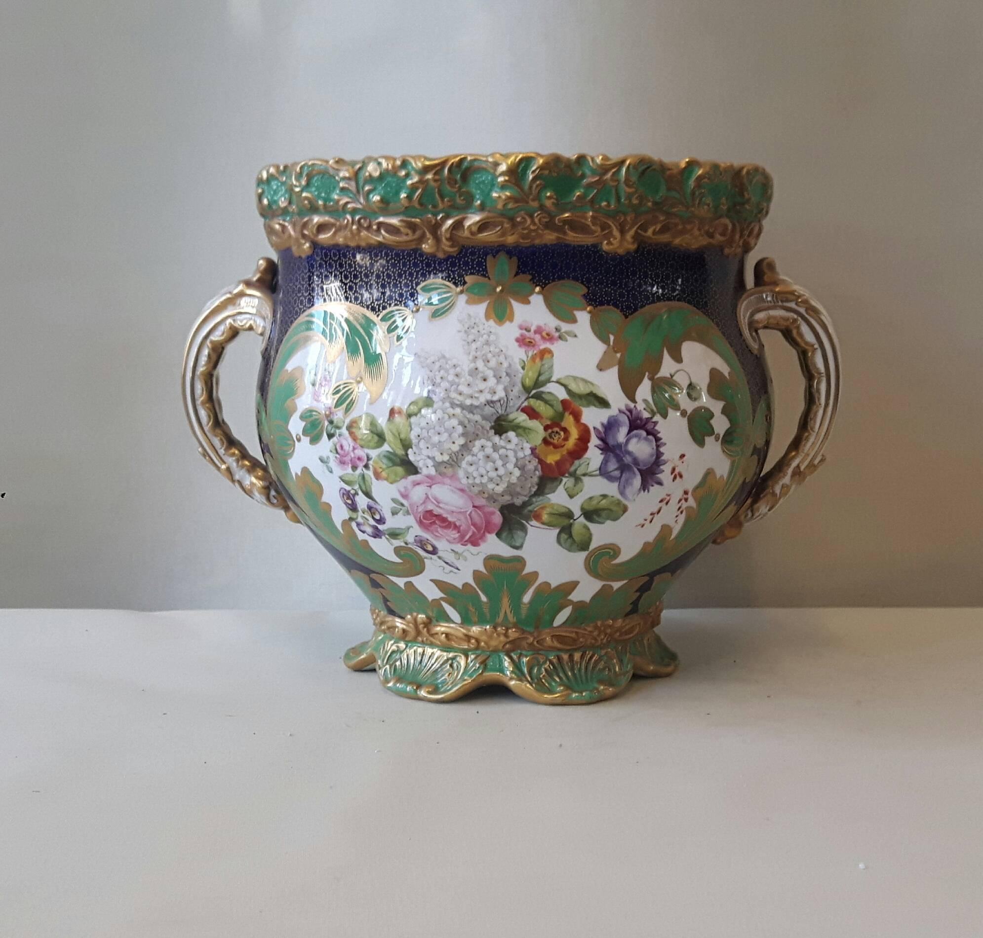 Un joli cache-pot Copeland, peint à la main avec des cartouches de fruits et de fleurs à la manière du 18e siècle, entourés de guirlandes de feuillage et de dorures. Le corps arrondi repose sur un rebord de style rococo

Le corps arrondi repose