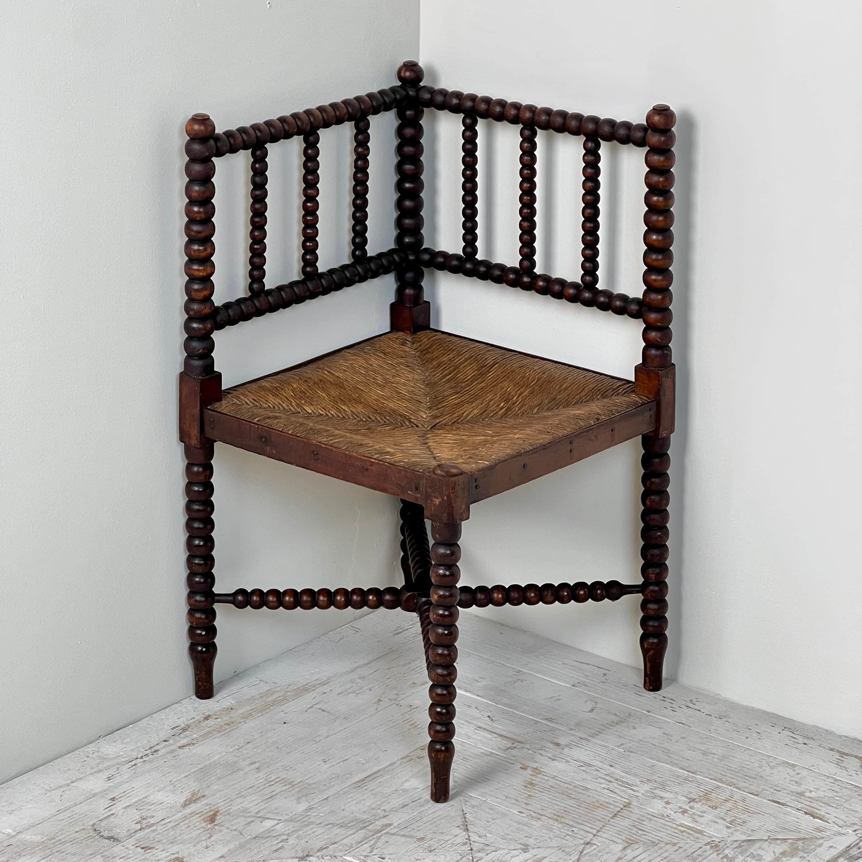 A Pretty Late 19th Century Corner Bobbin Chair With Rush Seat. Having turned bobbin uprights capped with finials to its back. Matchings legs with stylish cross stretcher.  The rush seat has a lovely colour and is in very good condition. Seat height