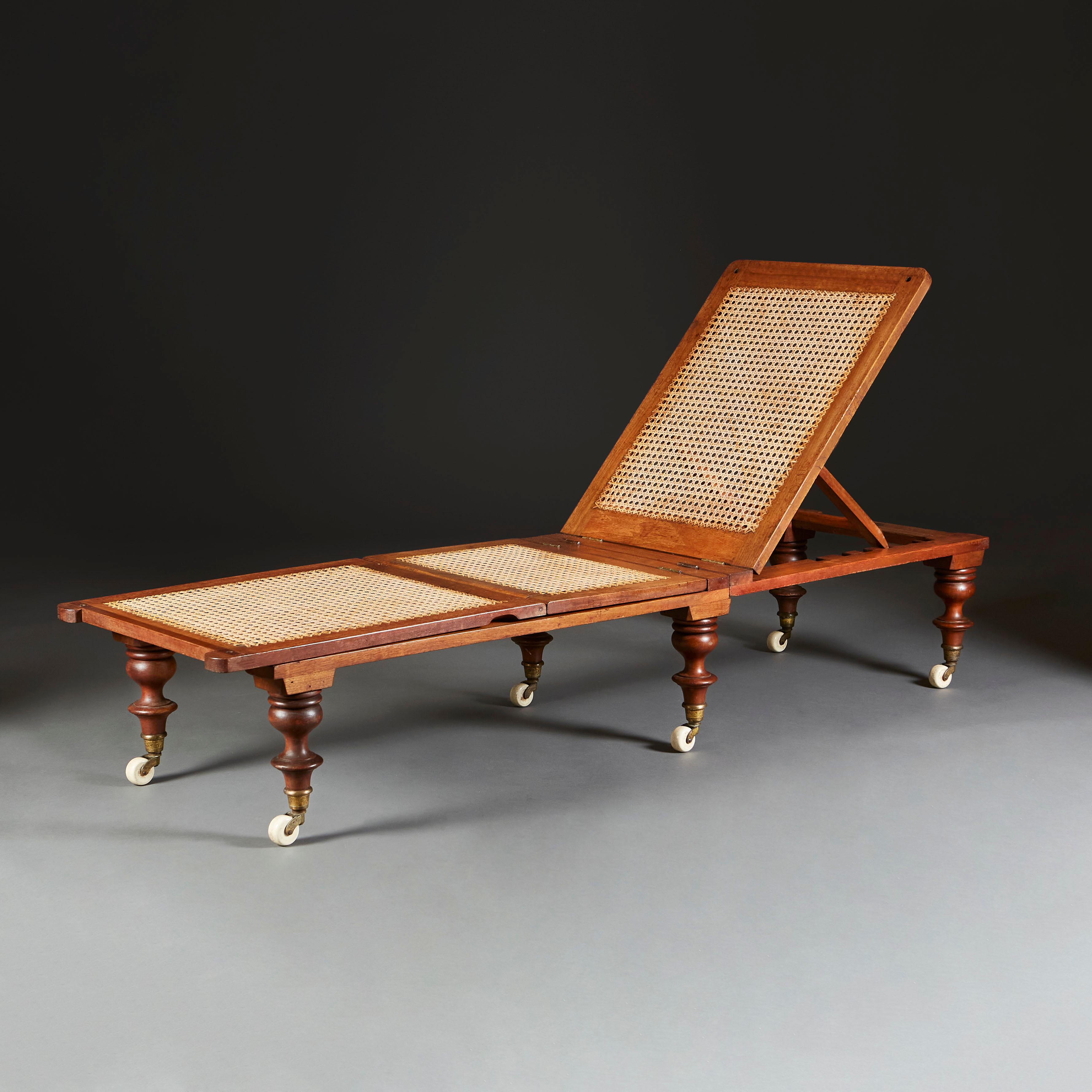 An unusual late nineteenth century mahogany day bed of articulated form, with adjustable back and leg splats, with caned seat, now with contemporary upholstered red and white striped cushions, all supported on turned legs with porcelain castors.