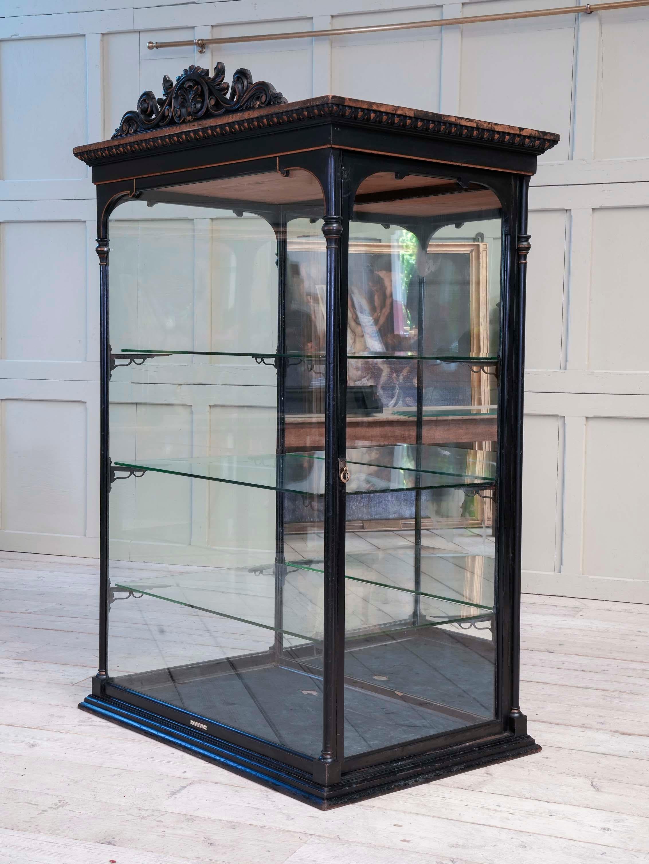 An outstanding full size ebonised and mirror backed retail display cabinet by Parnall & Sons of Bristol.

The three sided glazed case with ornate carved timber pediment above the egg and dart cornice all with its untouched painted decoration, the