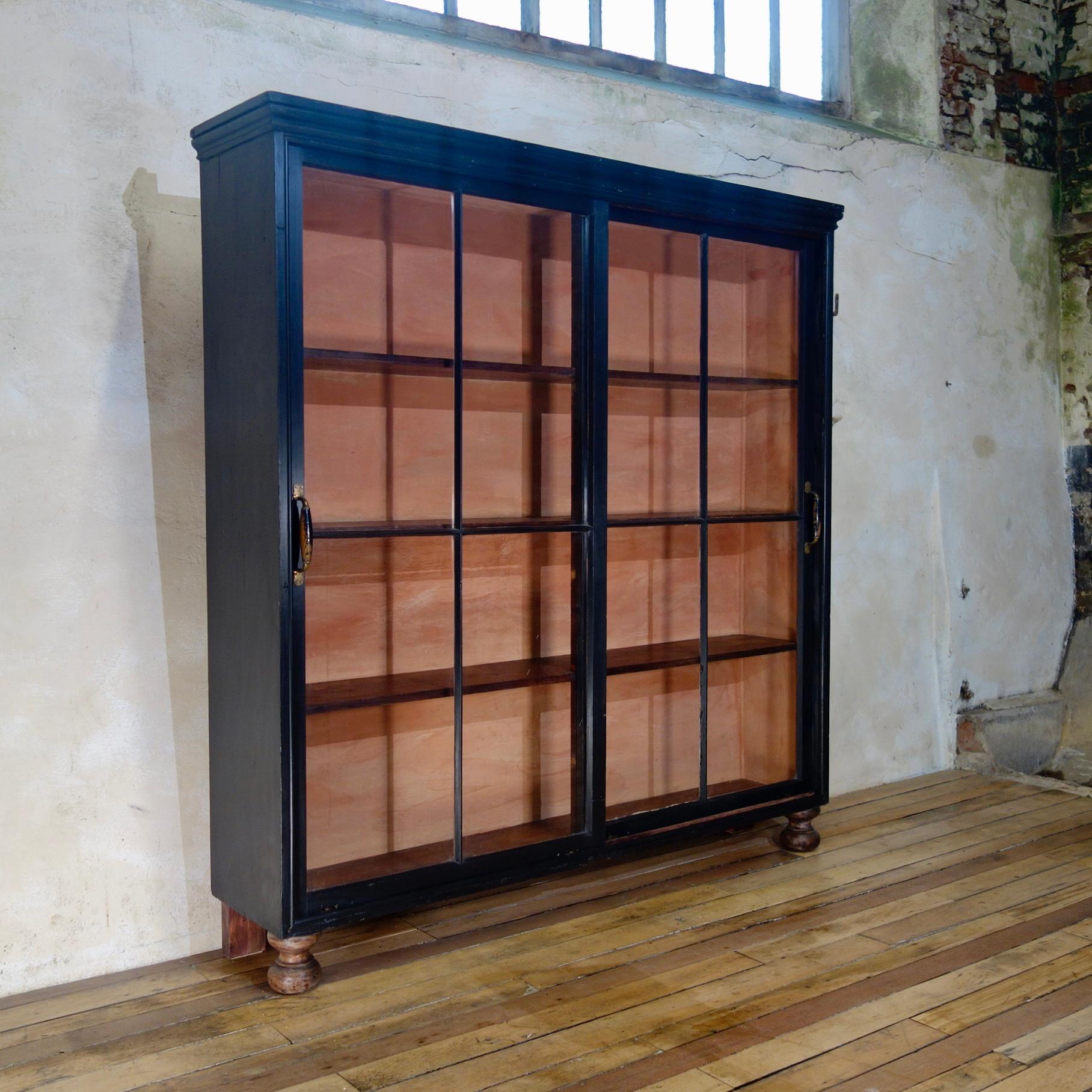 A unique late 19th century ebonized sliding door apothecary cabinet. Featuring a large pair of glazed doors, demonstrating it's original glass, enclosing a painted interior, raised on turned bun-like feet. 
 
Measures: Height - 190cm 
Width -