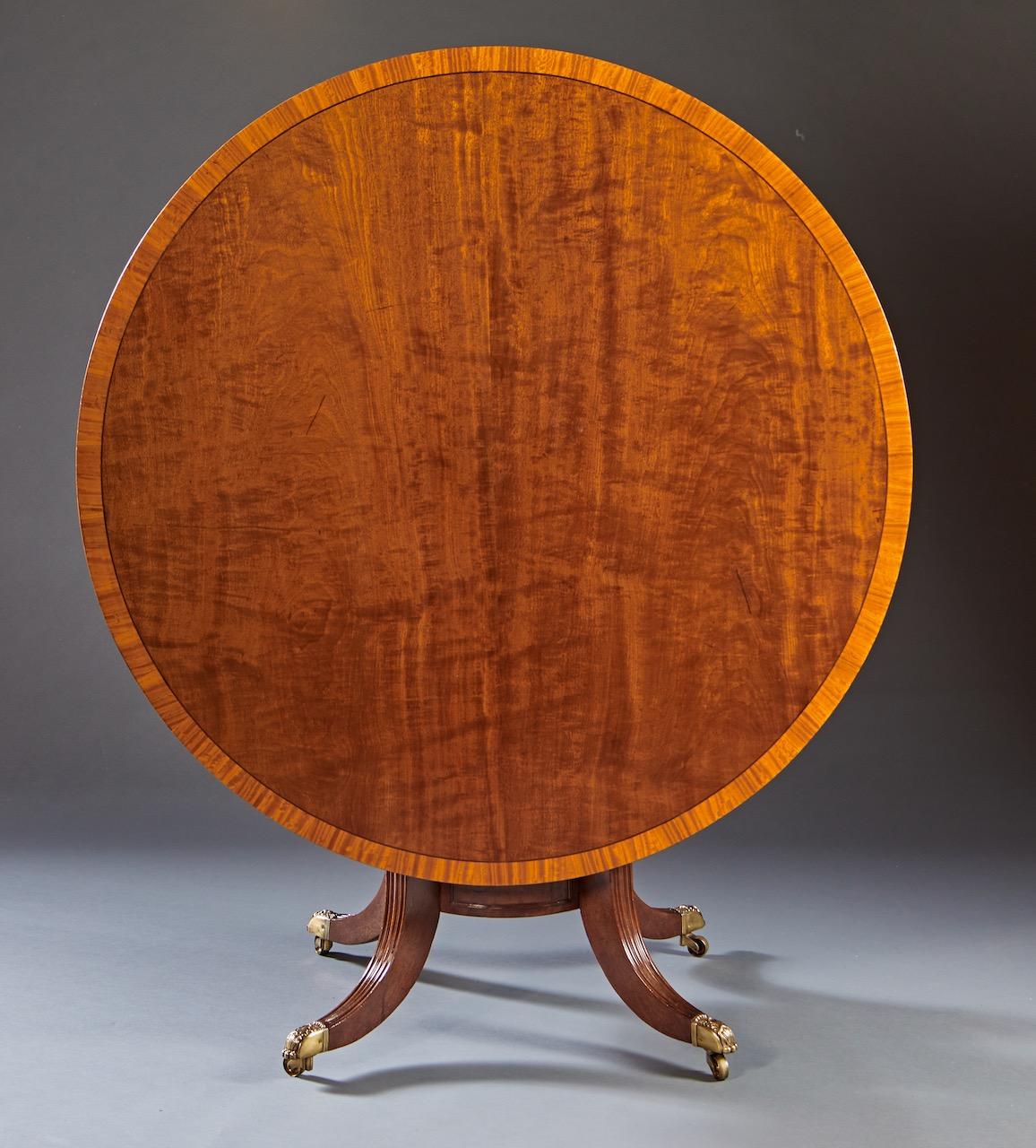 An engaging George IV period center table in choice mahogany with tilting mechanism. The figural round top is cross banded with a carved lozenge under molding. The top is supported by a turned shaft atop a circular platform raised on four molded