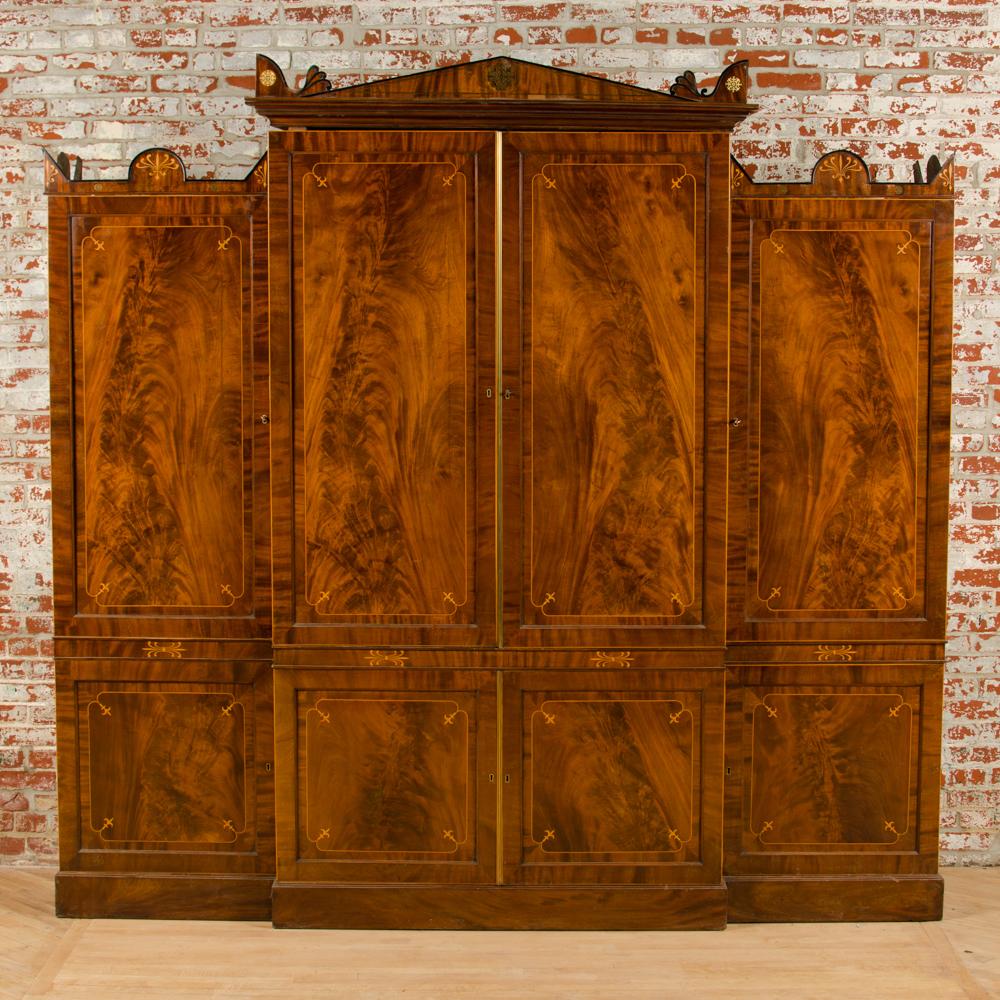 An imposing 19th century English Regency inlaid mahogany breakfront cabinet. The unit consists of two large central doors opening to six slide out shelves. Below are two small doors opening to reveal a full set of drawers. The left door is a full