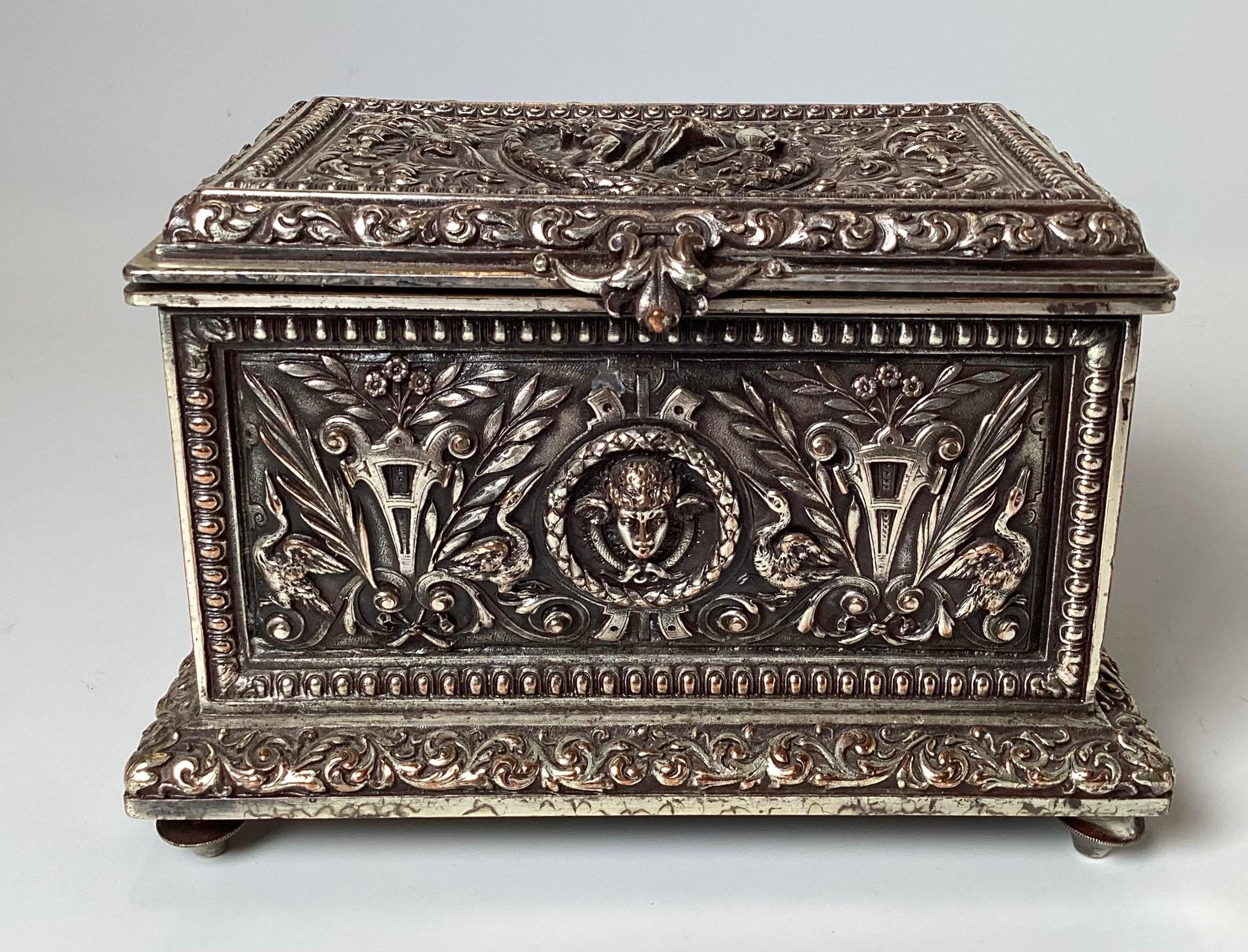 A silver plate high relived table box with hinged lid. The box is decorated with egrets, winged cherubs faces and classical scenes. almost 6 inches wide, 4 inches deep, 4.5 inches high.