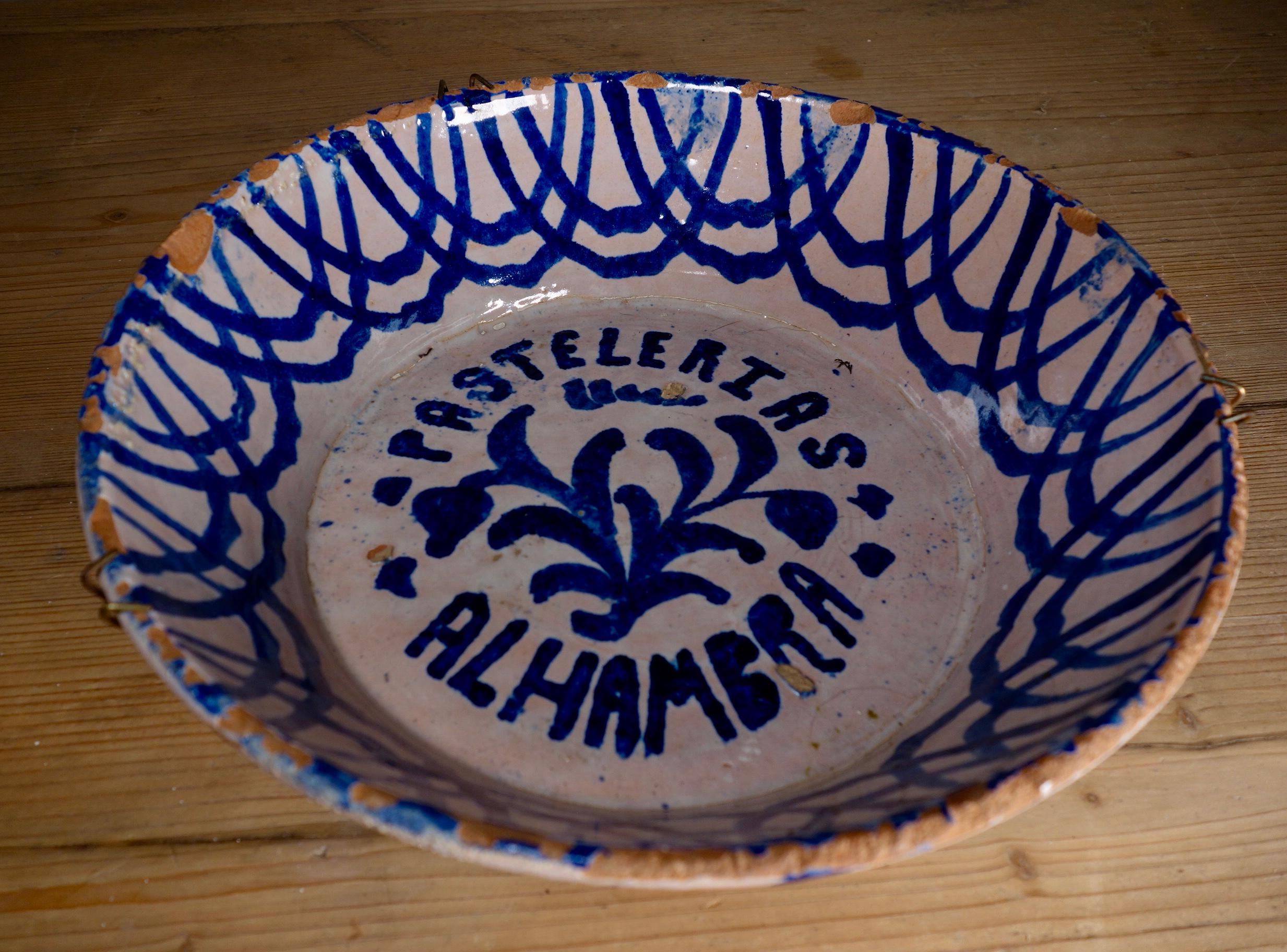 A 19th century Spanish bowl originating from Granada. This bowl has been decorated with blue hand painted decorations featuring 'Pastelerias Alhambra' written on the bottom of the bowl finished with overlapping semi-circular designs to the rim. 
