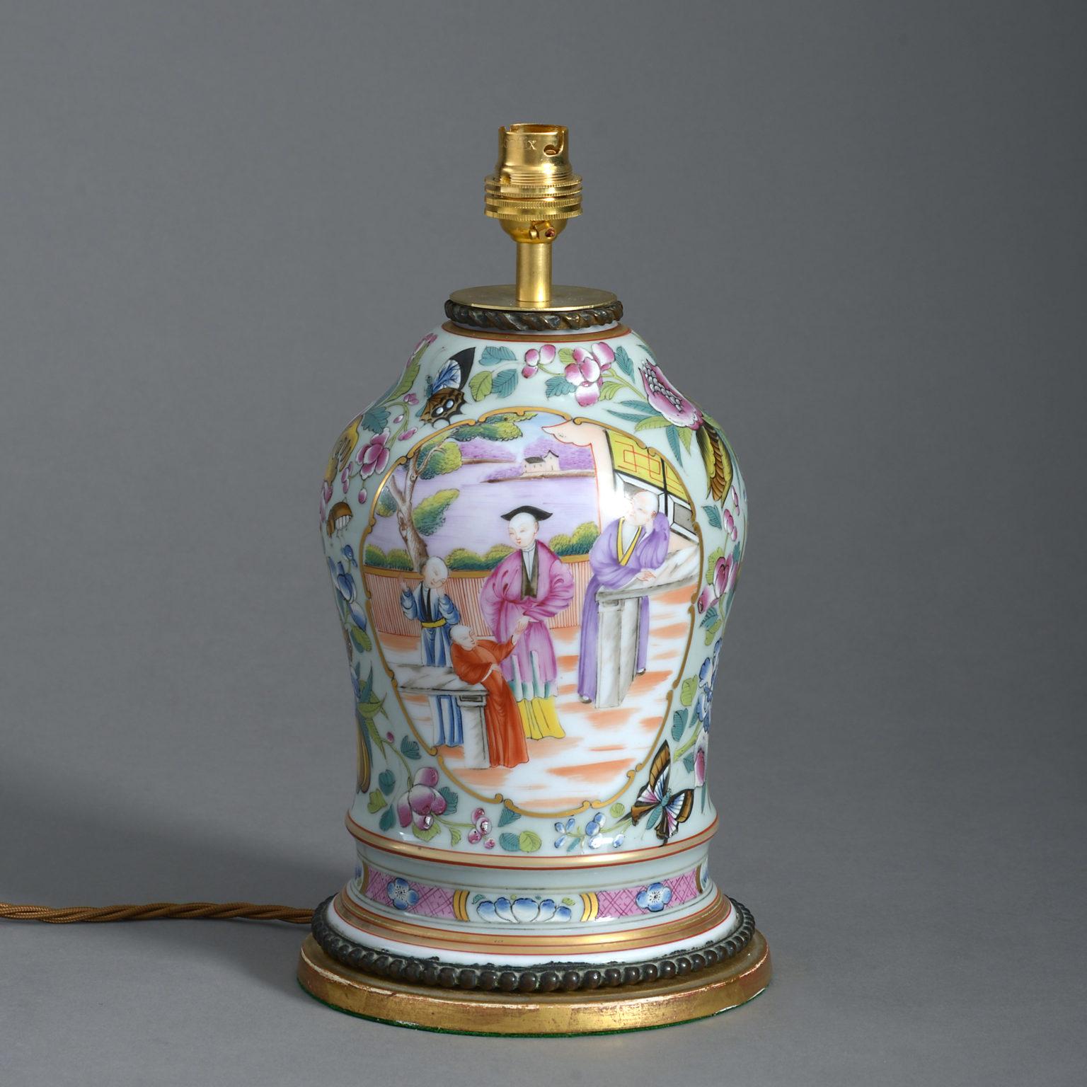A late 19th century famille rose porcelain vase, decorated with figurative cartouches, set upon a ground of stylised insects and butterflies. Mounted on a gilded base.

Dimensions refer to vase and base, excluding electrical components.

Shade