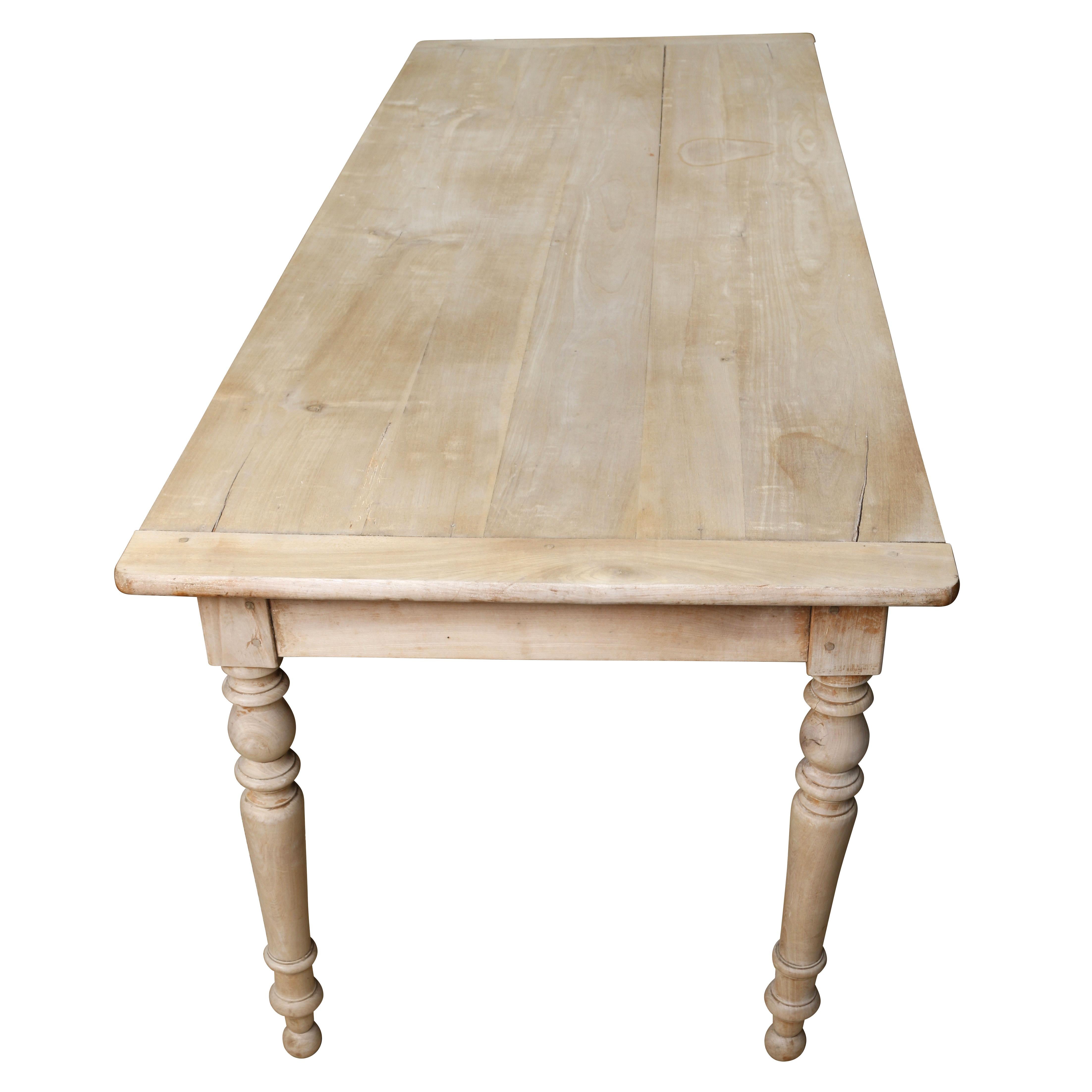 A charming bleached pine wood French dining table with one drawer. The top constructed of several long planks running the length of the table, with two planks at each end. It is raised on turned legs with nice detail. It's bleached finish gives it a