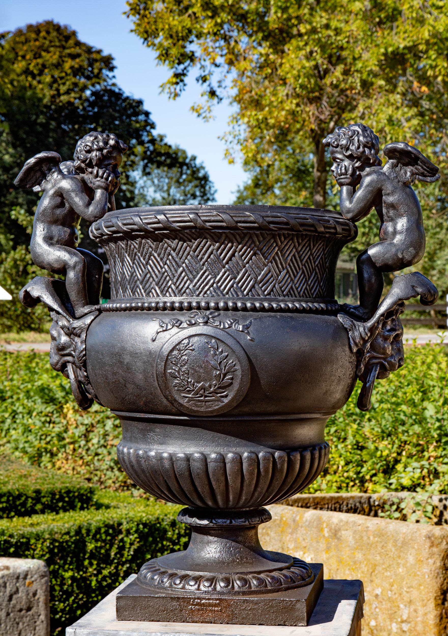 Urne en fonte française de la fin du XIXe siècle, coulée par A. Durenne, d'après Claude Ballin I (1615-1678). Le corps ovoïde et partiellement lobé, avec une bordure en treillis, est flanqué de deux poignées en forme de putti et repose sur un socle
