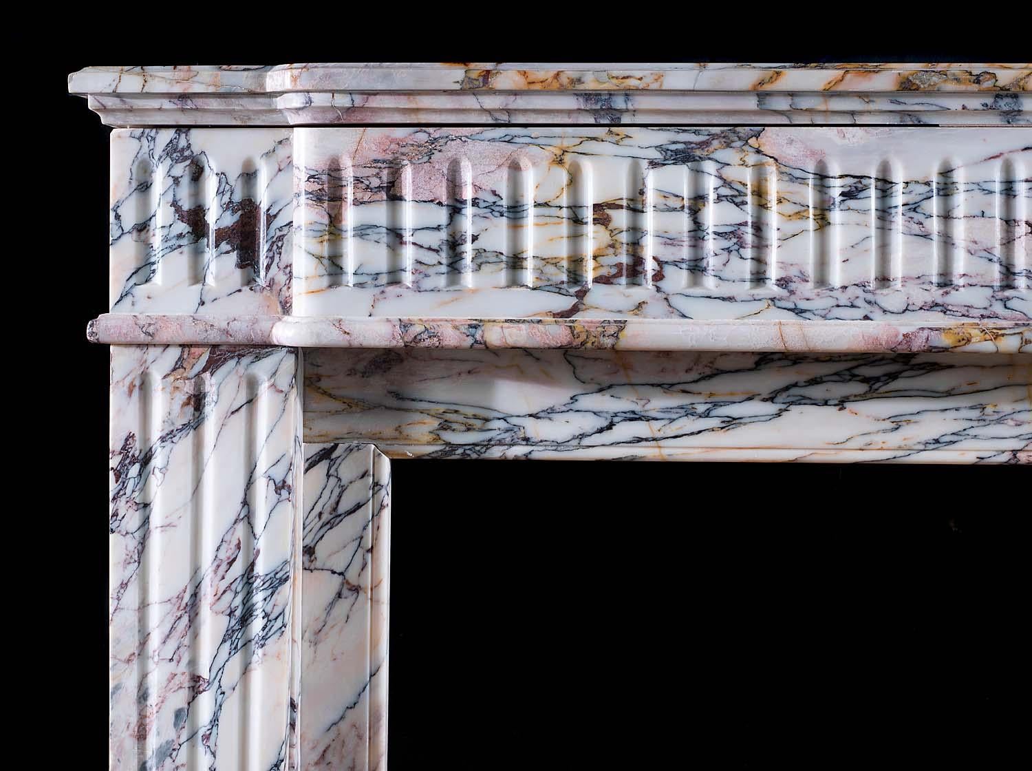 A Louis XVI style antique fire surround in rare Breche Violette marble with fine violet, rose, blue and gold veining on a white background. The breakfront shelf, with a moulded edge, rests above a wide fluted frieze flanked by fluted end blocks