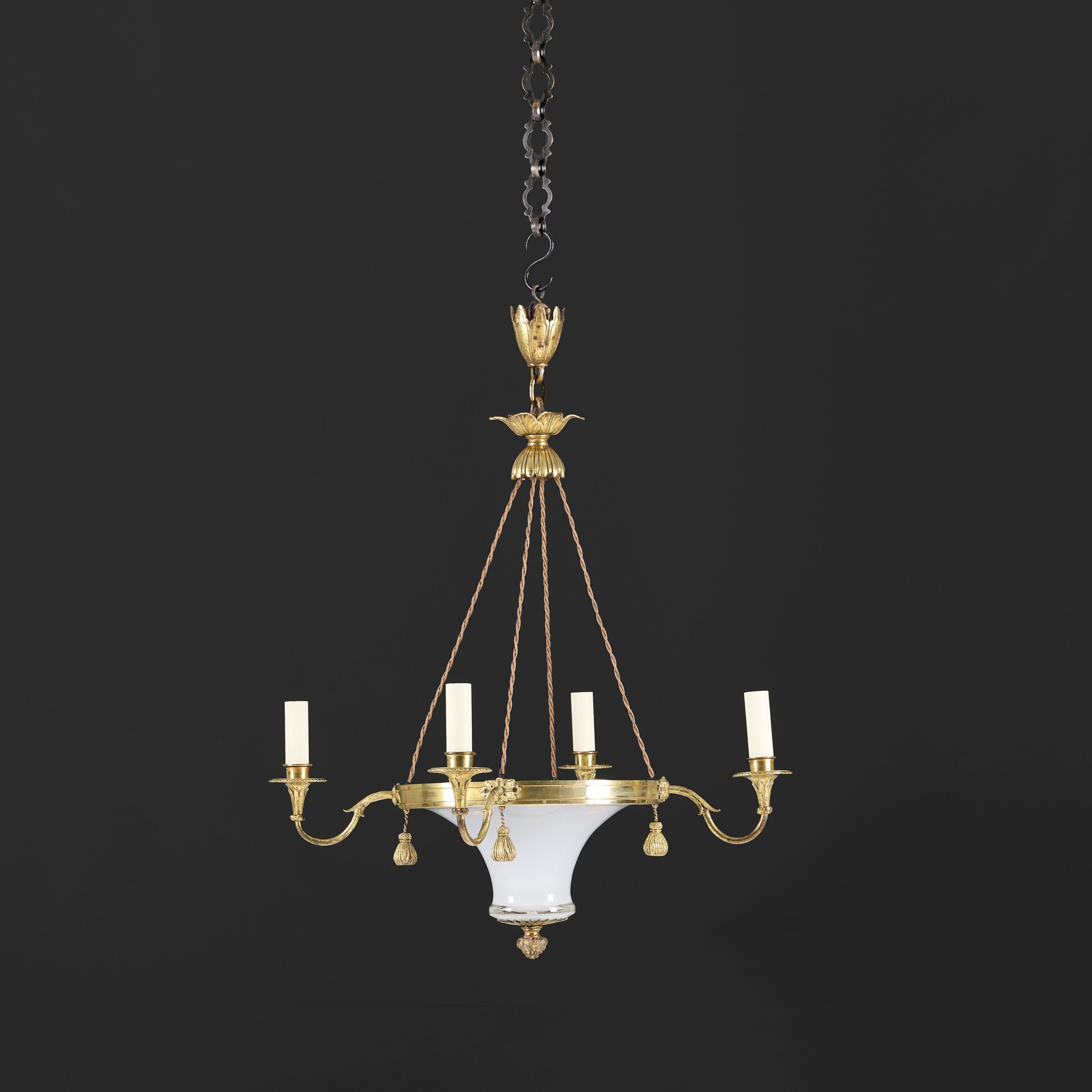 Francia, circa 1860

A French mid-nineteenth century chandelier with central opaline glass dish mounted by four ormolu candle arms with flared drip trays and hanging tassels, terminating in an acorn finial with foliate skirt and matching ceiling