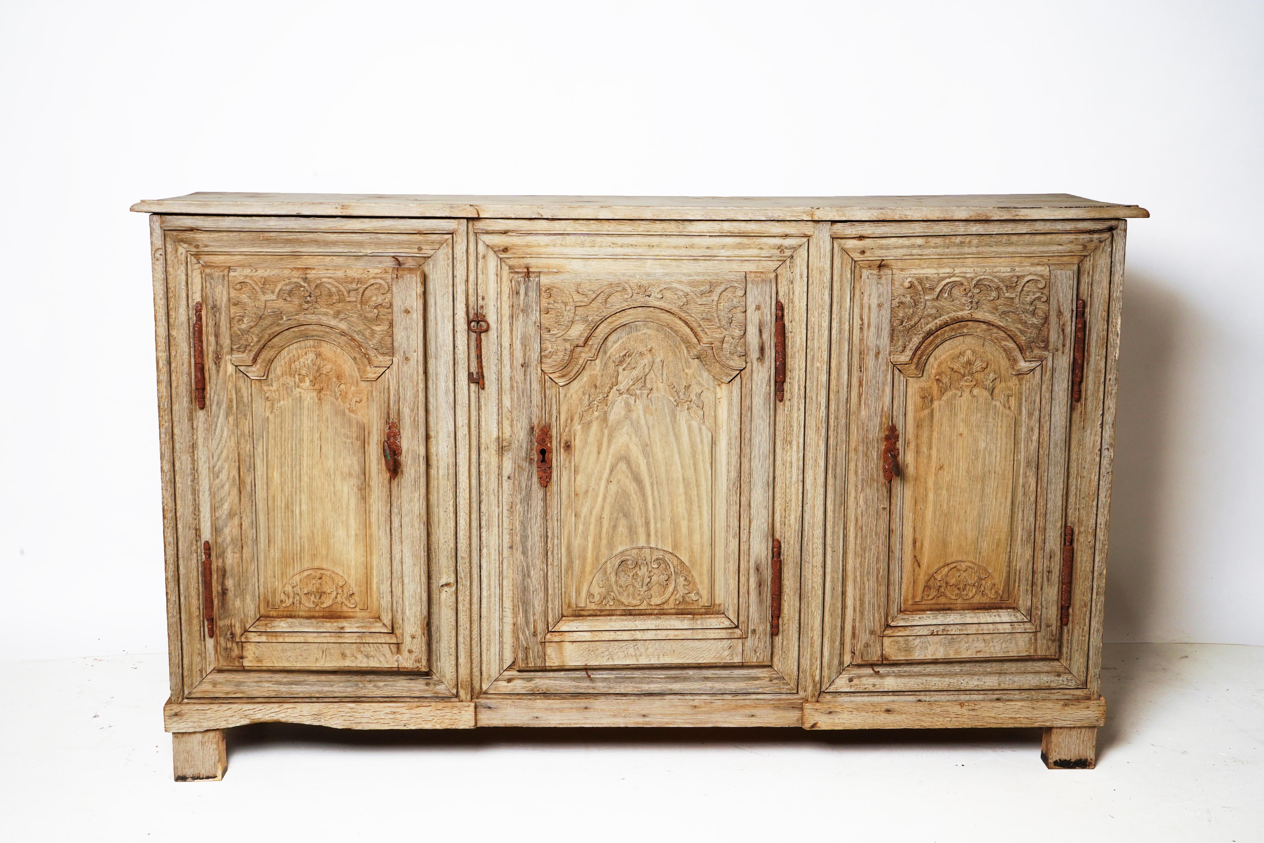 This smaller-scale French sideboard is made from white oak and features finely-carved scrollwork on the doors. Hinges are original. The piece has been stripped, scrubbed and bleached. The piece is Provencal in origin.