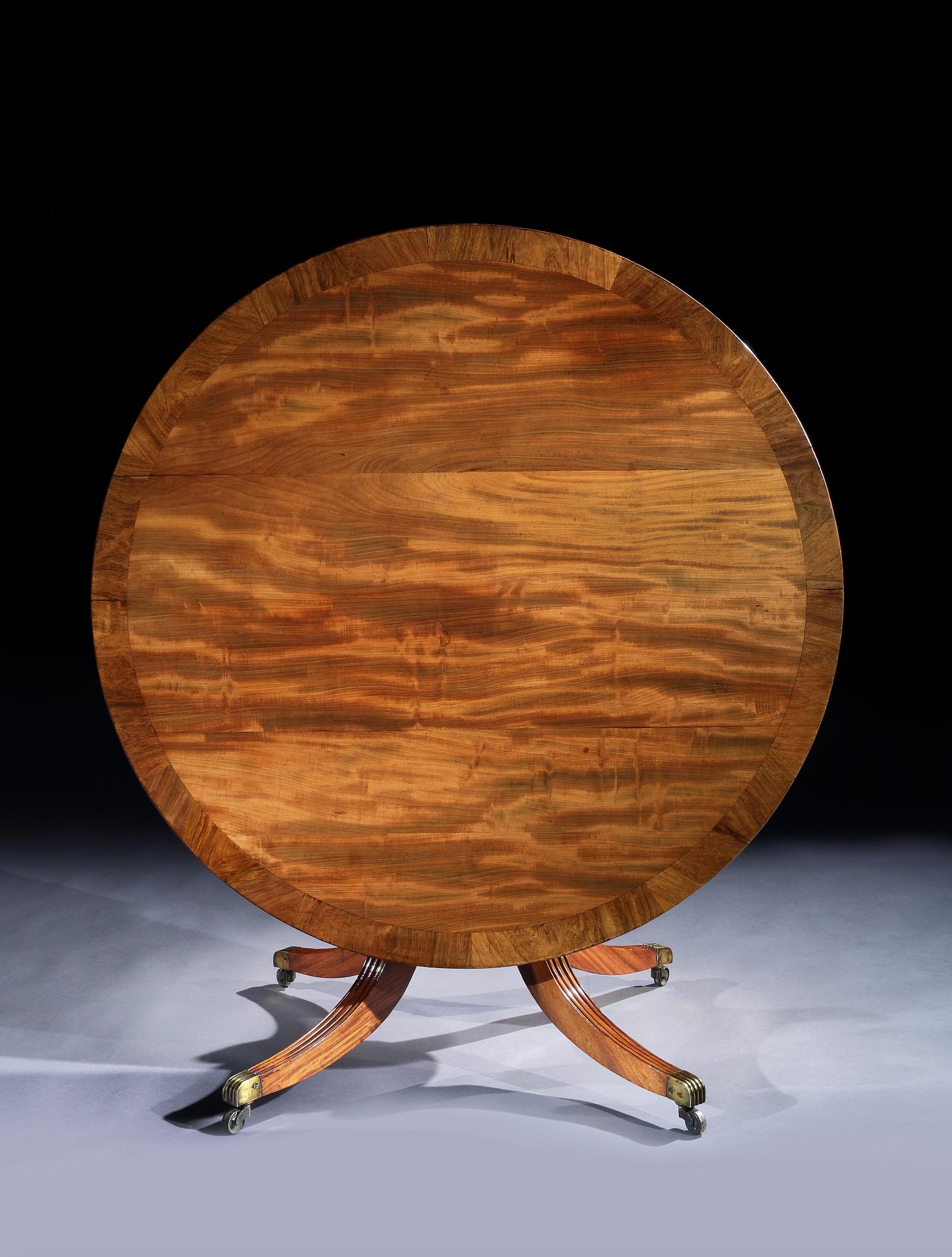 A fine early 19th century mahogany breakfast or centre table. The circular top with a wide mahogany cross-baned border, on a central turned pedestal support with four hipped outsplayed reeded legs, terminating in brass castors.

Of good colour