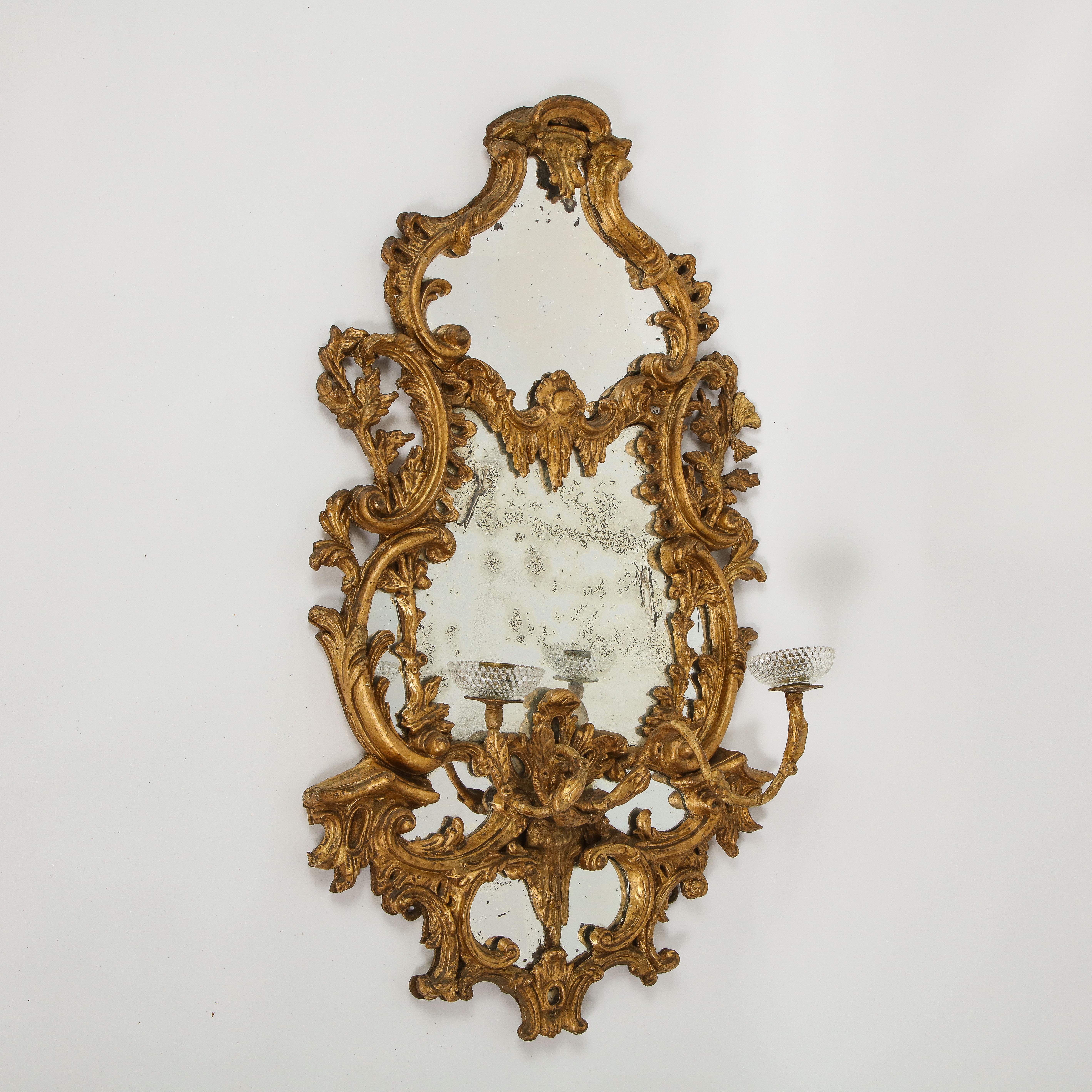 The cartouche-shaped frame elaborately molded with foliate C-scrolls, cabochons, and rocaille decoration; issuing two outward scrolling candlers with cut crystal drip pans.