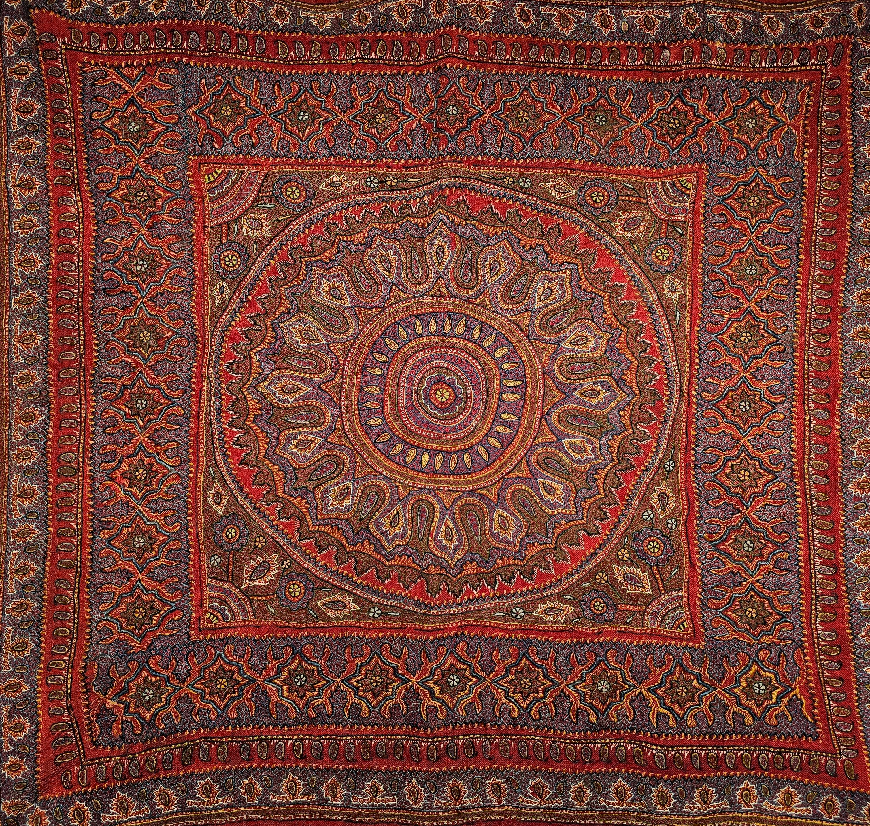 Die charakteristische persische Kerman-Suzani (Termeh-Stickerei auf Persisch) stammt aus der alten Stadt Kerman in Persien. Der handgestickte Wandteppich ist auf einem roten Stoffgrund mit Stickereimustern in Blau, Lila, Gelb und Braun. Das