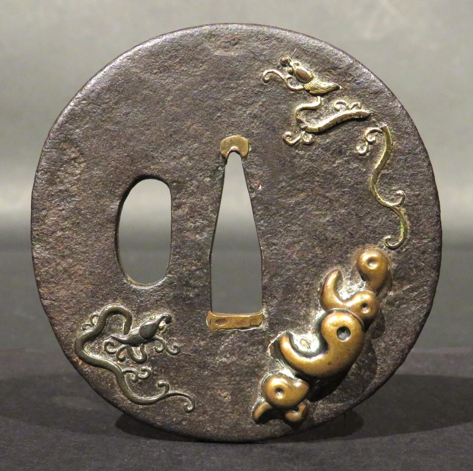 A finely decorated iron & mixed metal tsuba, showing a dark-brown iron ground decorated in low relief with organic inspired motifs in gold, silver & copper.