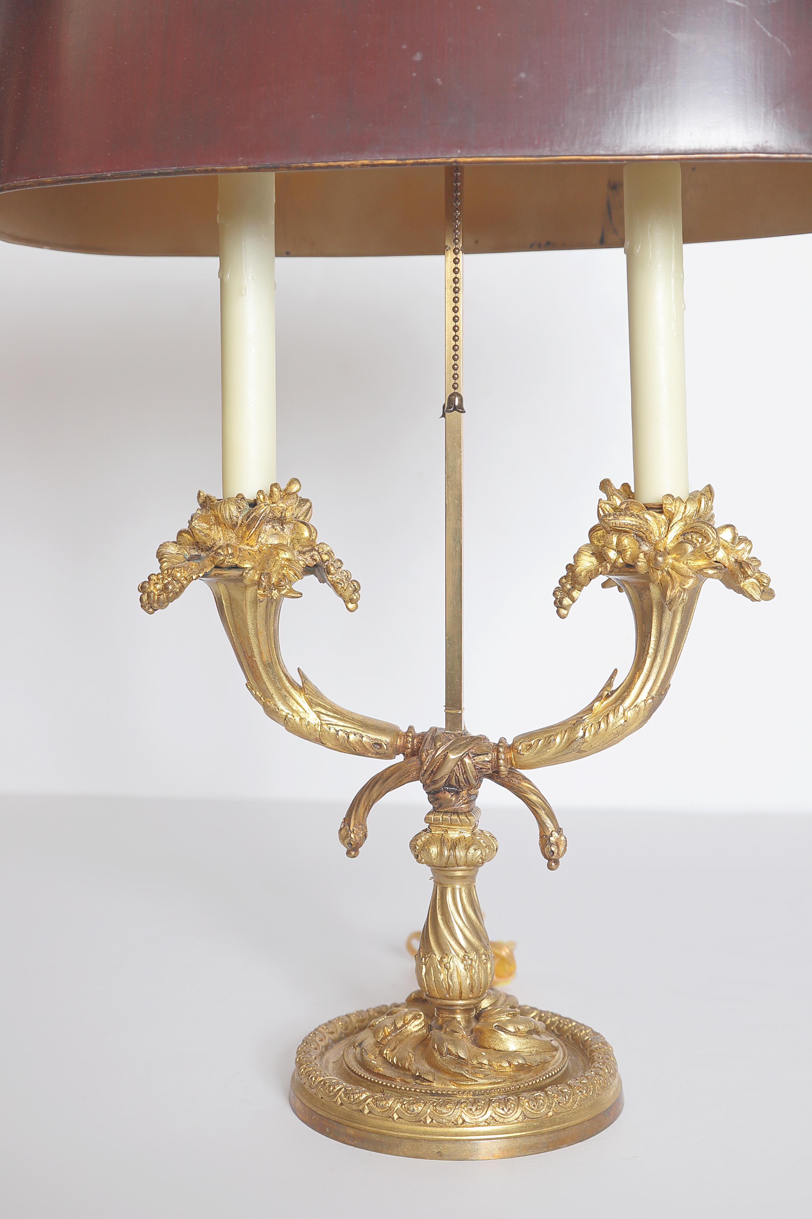 A 19th century Louis XVI style ormolu bouillotte lamp with red tole shade, the shade over two foliated arms rising on a circular base with beading and floral molding. Second half of the 19th century. (Old repairs).