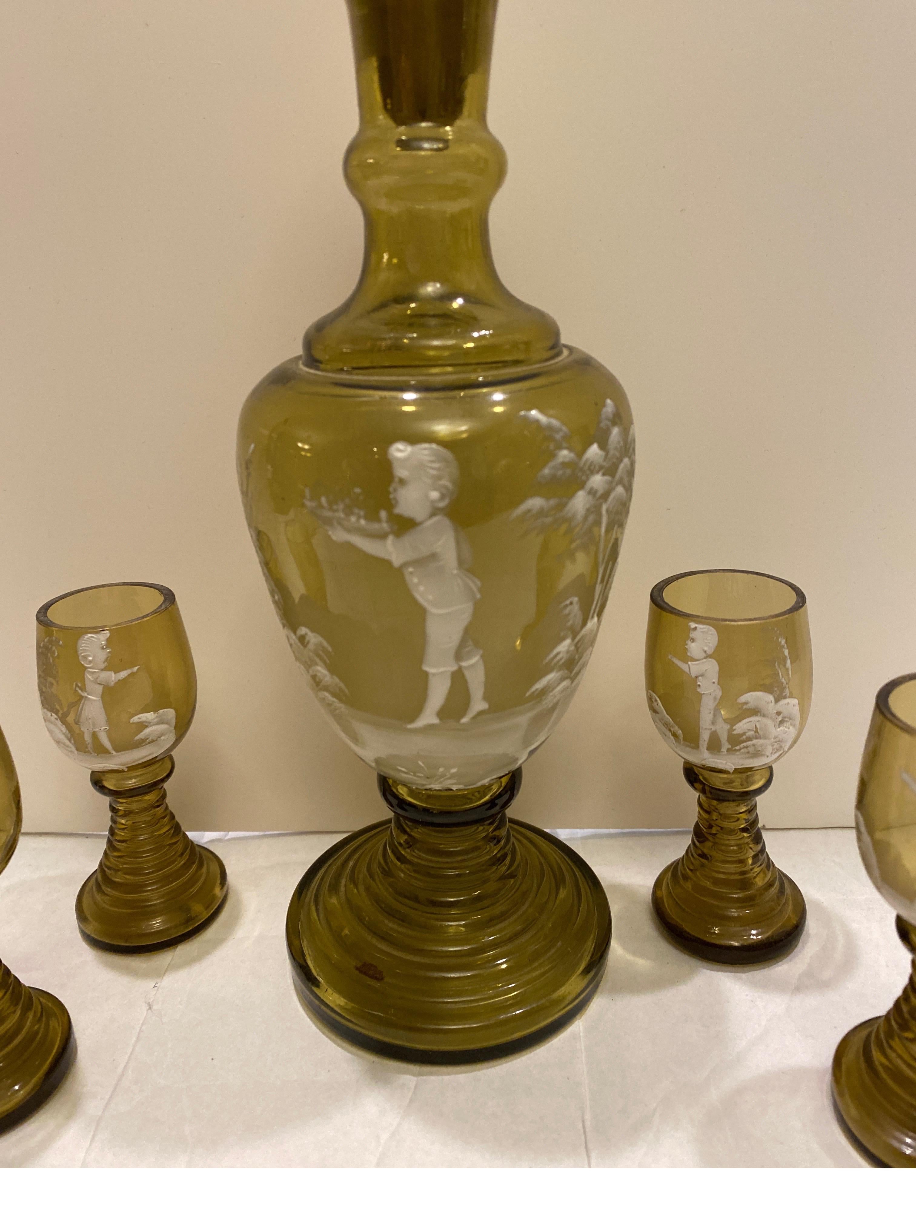 A charming decanter and glass set in moss green Mary Gregory glass. The hand-blown forms with hand enameling in classic Mary Gregory decoration. The decanter with original stopper is 11 inches tall, the glasses are 3.5 inches tall.