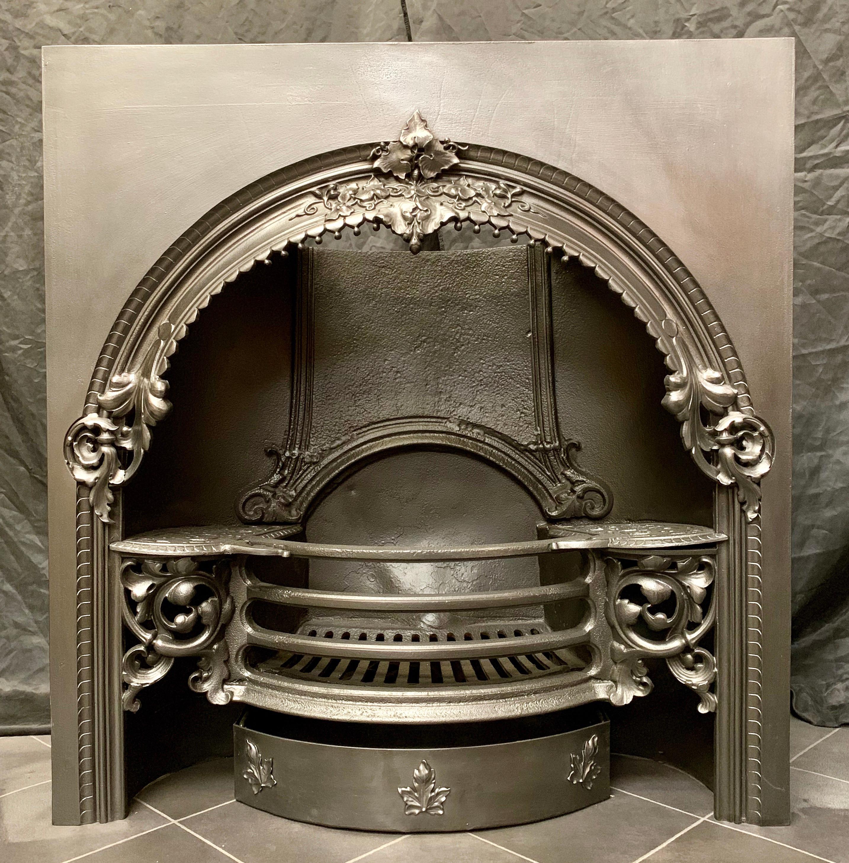 A large and ornate 19th century mid Victorian cast iron register fireplace insert in the Rococo manor, a large protruding sweeping arch with a highly decorated central cluster of leaf's and tendrils, a four bar fire grate, is flanked by further high