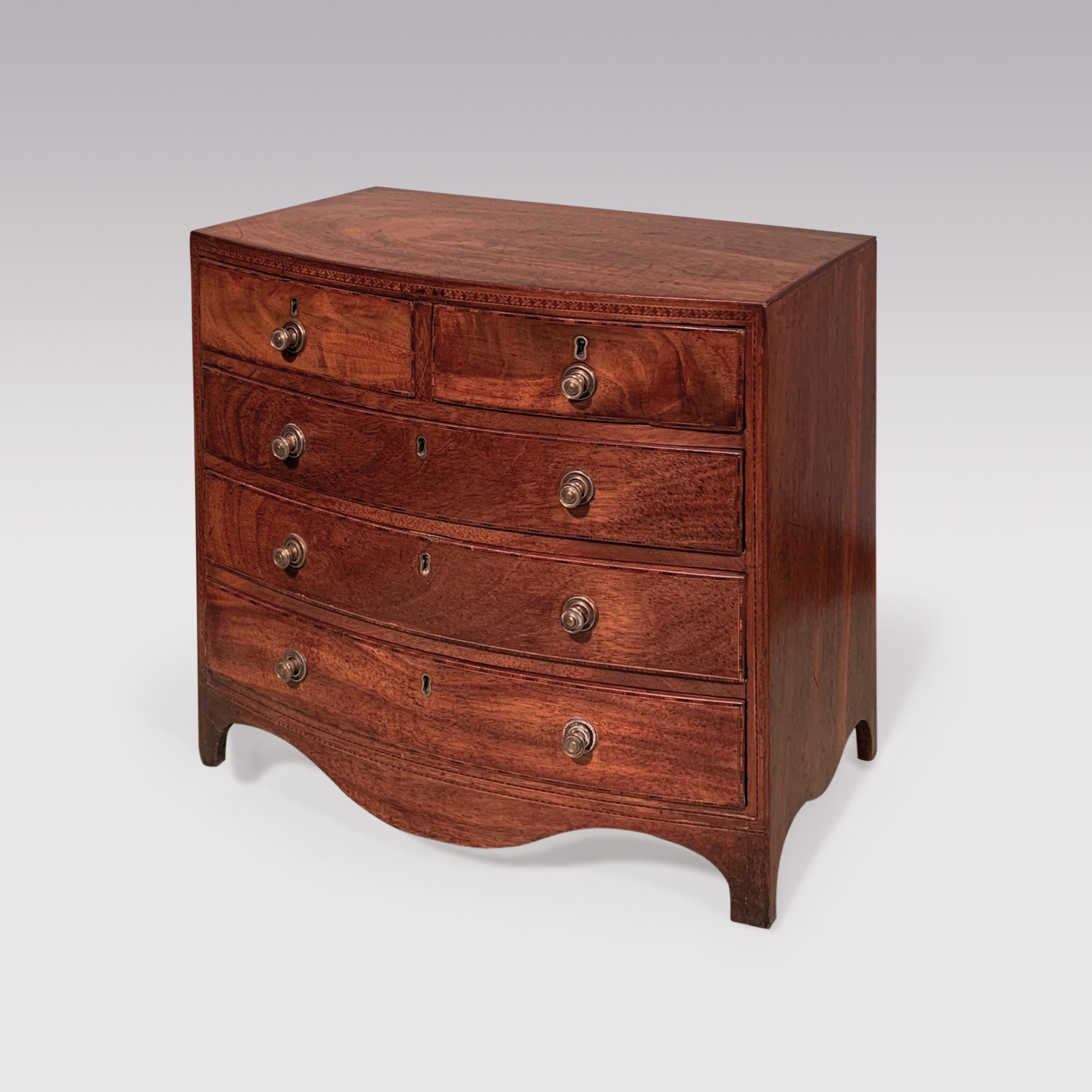 An early 19th century well-figured and faded mahogany miniature bowfront Chest of 2 short and 3 long graduated drawers. The Chest retaining original brass handles, with crosshatched inlay to the front, supported on bracket feet with shaped apron.