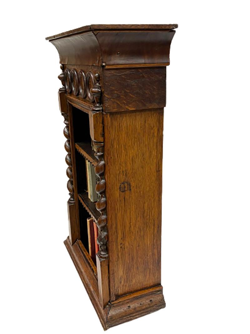 A 19th century miniature wooden bookcase

An oak miniature bookcase, raised on plinth and 2 charming shelves. (2 loose shelves) Decorated at the front with 4 rings between 2 twisted columns. At the top is a veneer layer, which is damaged and part