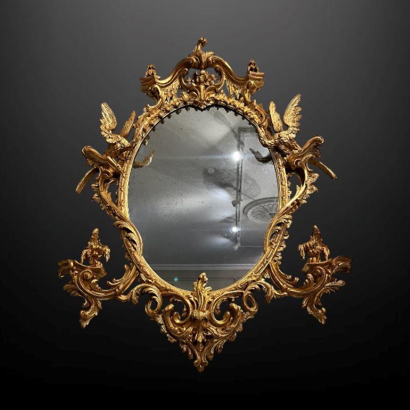 Miroir mural ovale du XIXe siècle à la manière de Thomas Johnson, dont l'exubérance dramatique du design a été habilement tempérée et équilibrée pour présenter une pièce des plus enchanteresses.

La crête feuillagée est soutenue par des rinceaux en