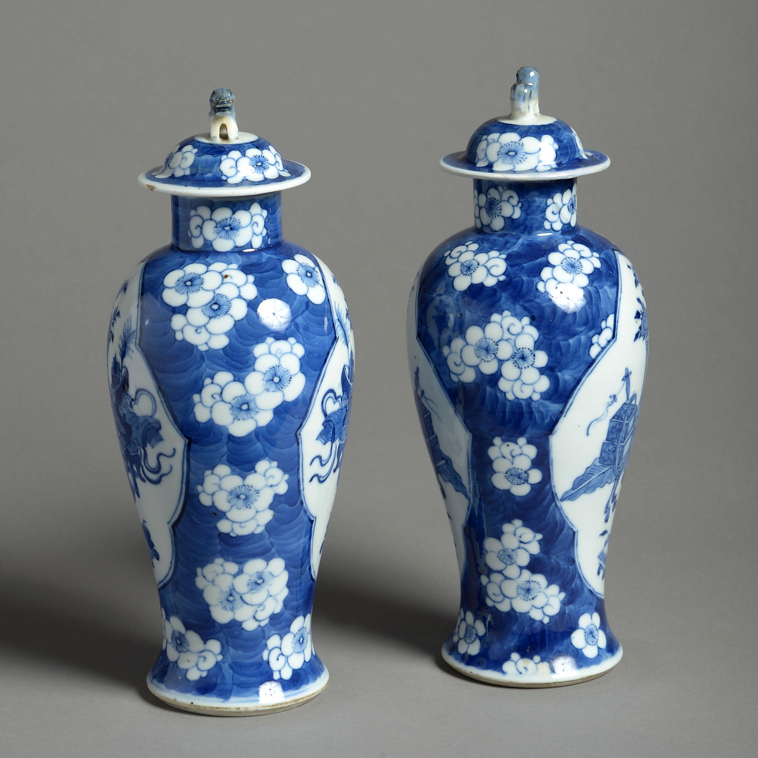 A pair of 19t century porcelain vases and covers, both decorated with the hundred antiques motif, within cartouches, set upon a ground of prunus blossoms in blue and white glazes. 

circa 1860, China.