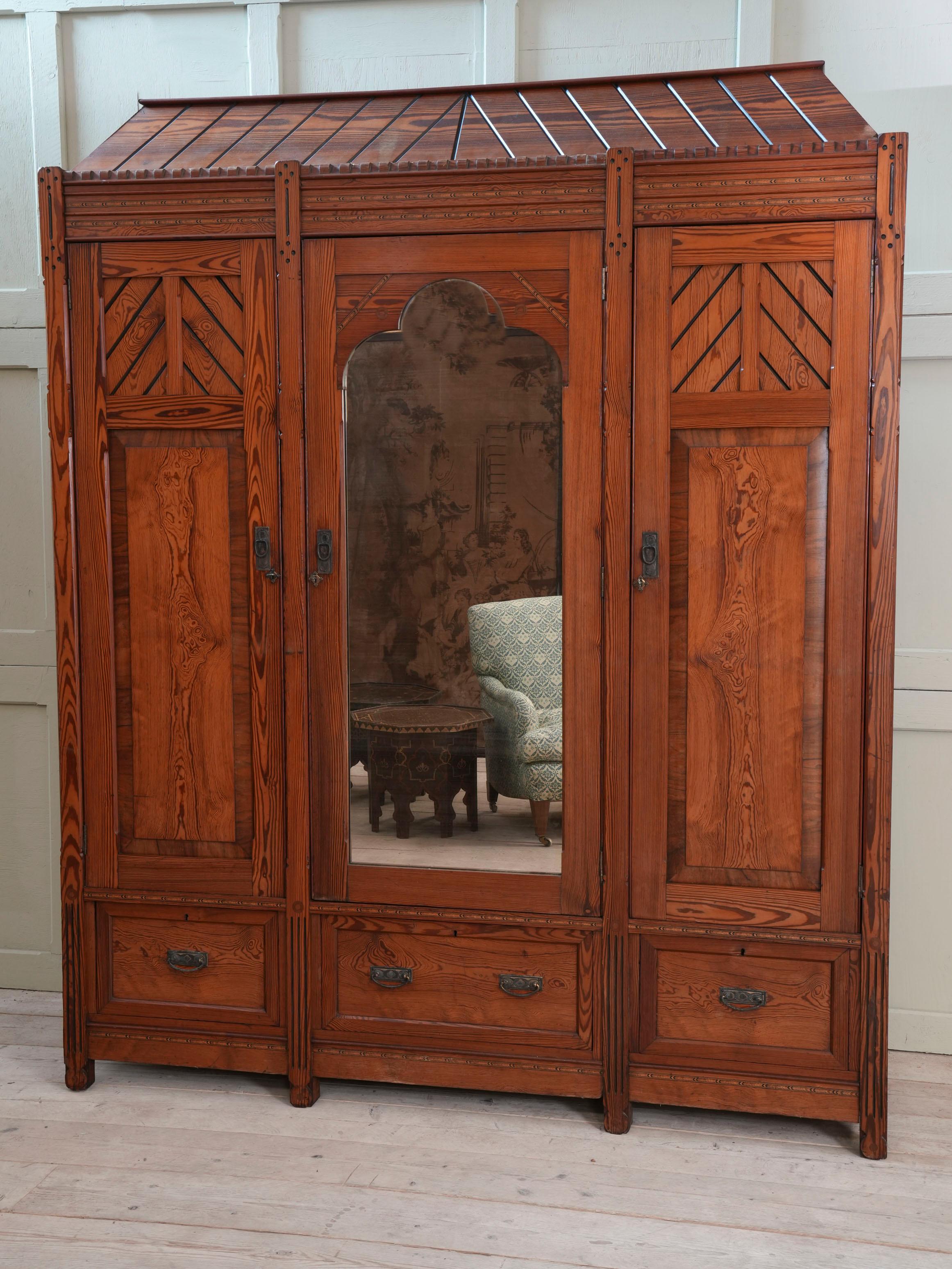Two solid doors with hanging space behind flank the central mirrored door with sliding shelves behind above three drawers to the base.

In the manner of John Pollard Seddon 1827-1906.