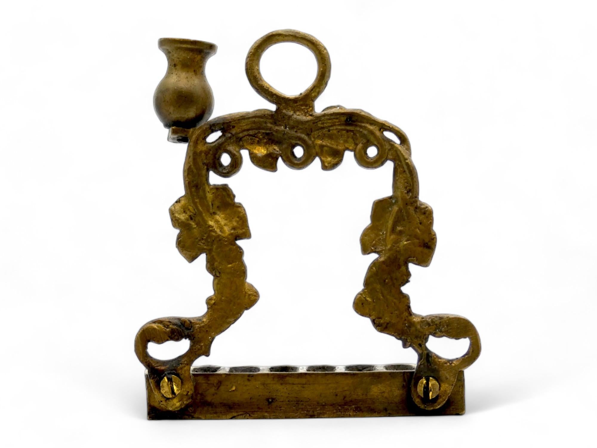 Lampada di Hanukkah in ottone del XIX secolo, realizzata in stile rococò.

La piastra posteriore traforata presenta corone floreali e di vite che si attorcigliano verso l'alto e che incorniciano il retro della lampada di Hanukkah.

Un anello