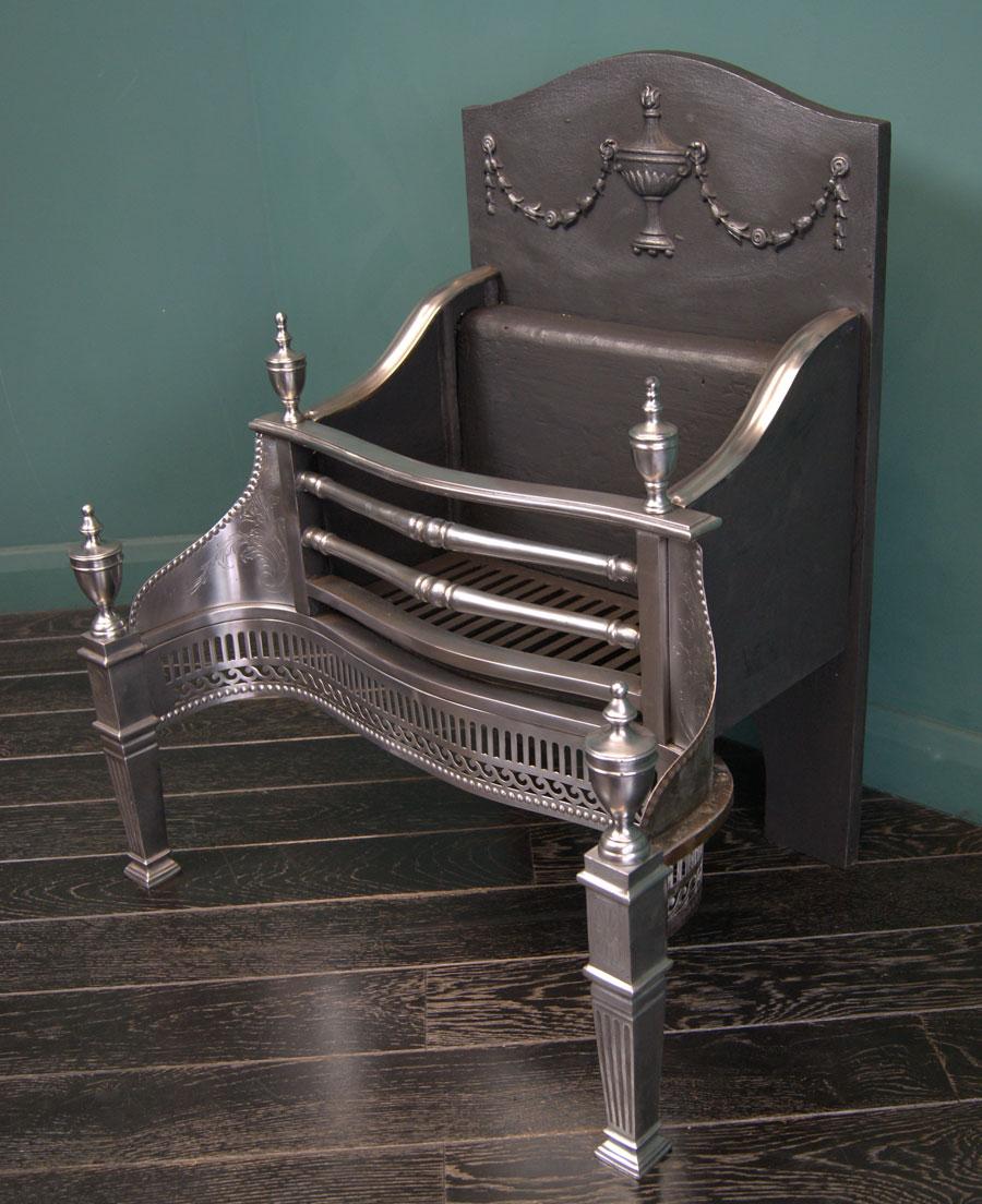 A sturdy polished steel fireplace fire grate in near perfect condition. The polished steel front with ornate fire bars, flanked by wings engraved with foliage over a fluted and s-scroll fret. Urn finials sit uppermost in front of an ornate cast fire