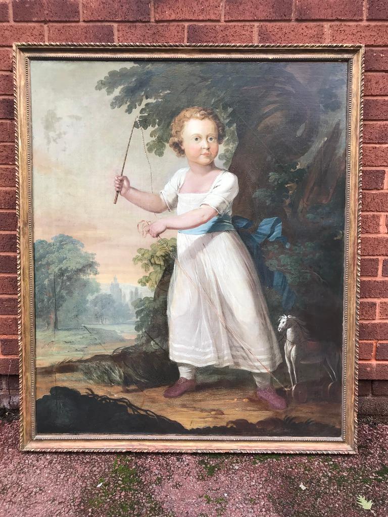 Porträt eines Jungen, der mit einem Holzpferd spielt, in einer schönen ländlichen Umgebung mit Laub und Bäumen. Präsentiert im originalen, handgeschnitzten und vergoldeten Rahmen.