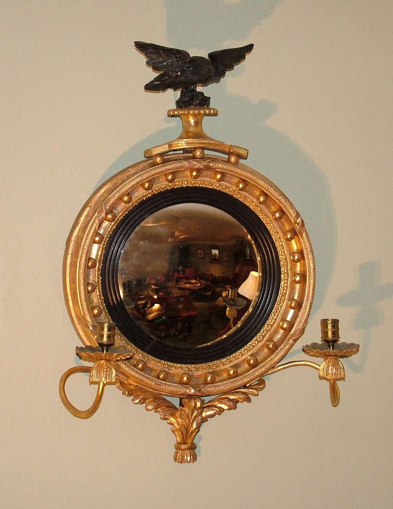 A small and attractive early 19th century Regency period carved giltwood convex mirror, having eagle pediment perched on platform above ball decorated moulded frame flanked by scroll candle-arms and acanthus leaf carving below.