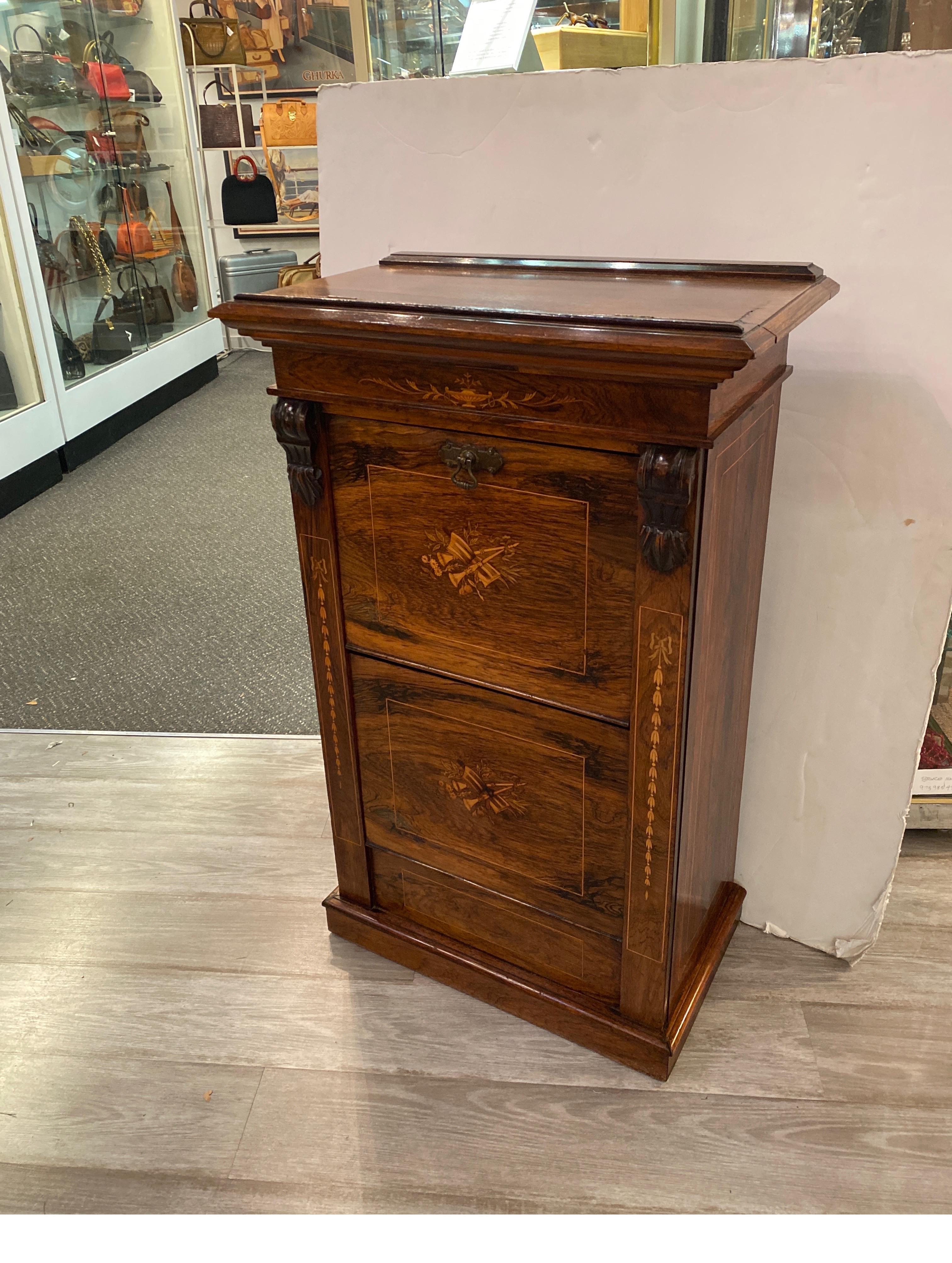 Sunning rosewood music cabinet with inlay of satinwood. The top with a lift up lectern shelf, the base with two doors that fall open to hold music, magazines or reading material. Elegant grained rosewood with carved top pilasters on each side and