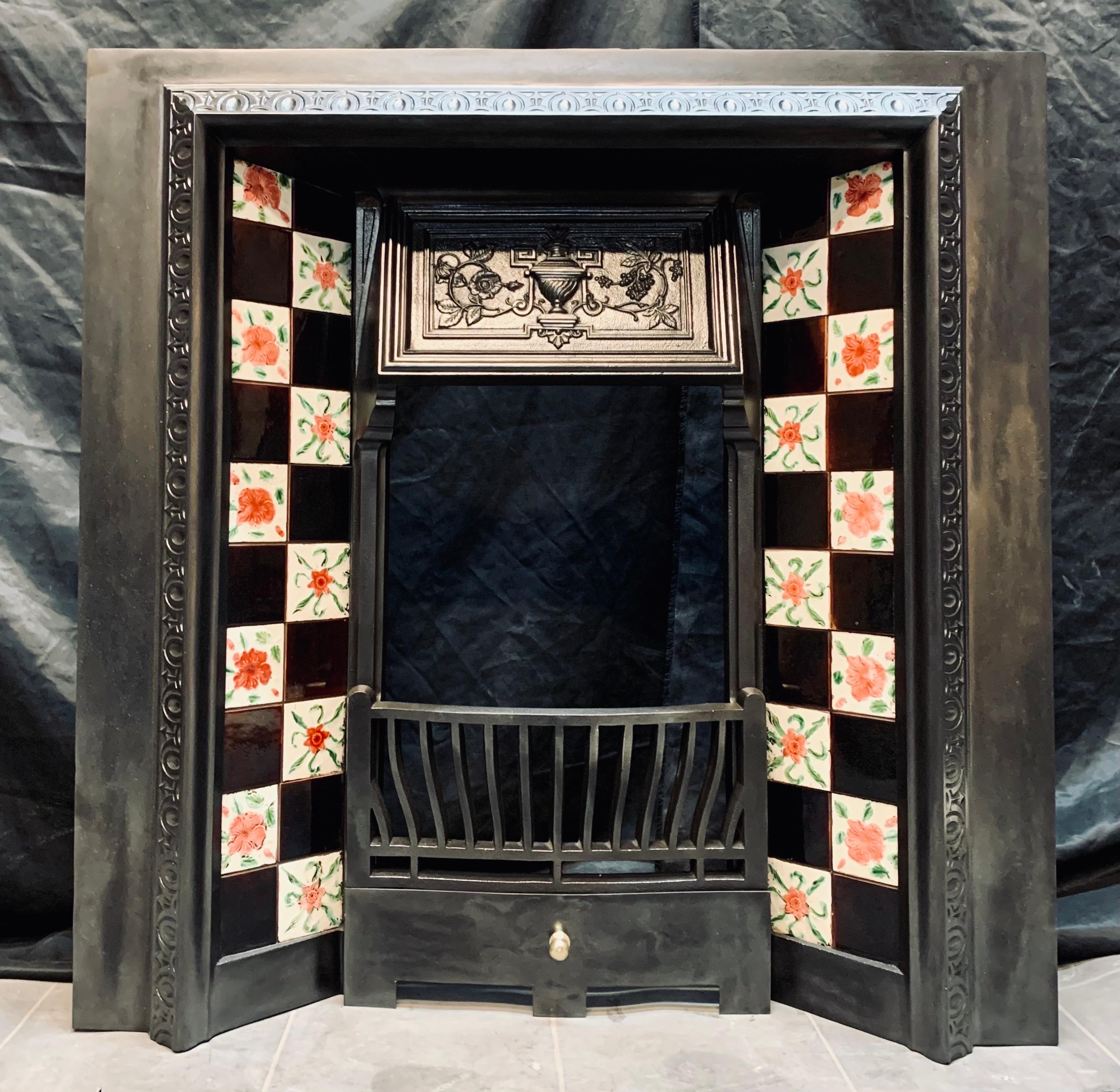 A Scottish 19th Century Victorian cast iron fireplace insert with hand painted original tiles. A cast iron outer frame with a raised decorative border, a central hooded canopy with high relief detail flanked by a pair of hand painted original tiles.