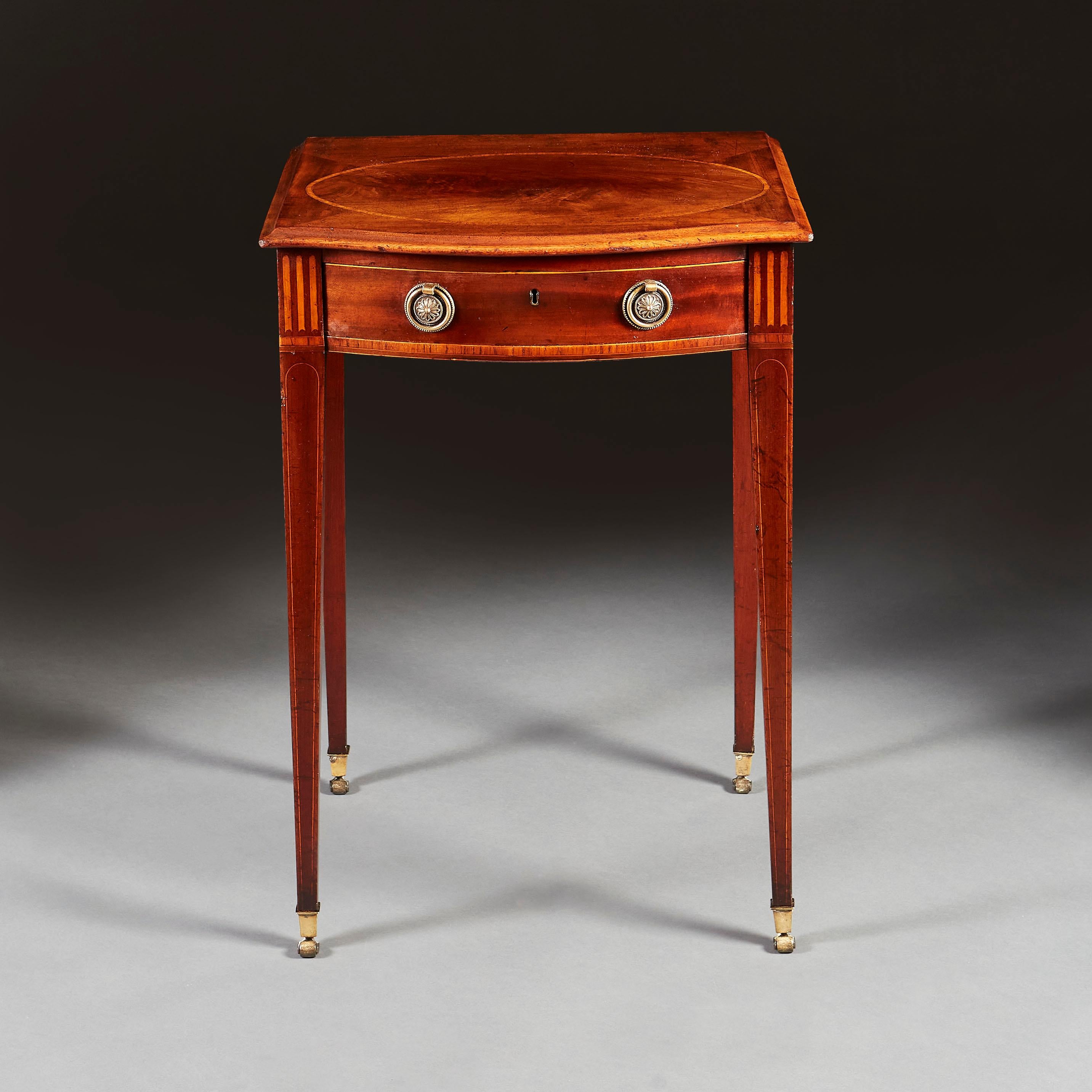 A late nineteenth century mahogany occasional table with serpentine shaped front, with satinwood stringing and a single drawer to the frieze, with brass paterae handles, all supported on four tapering legs terminating in brass castors.