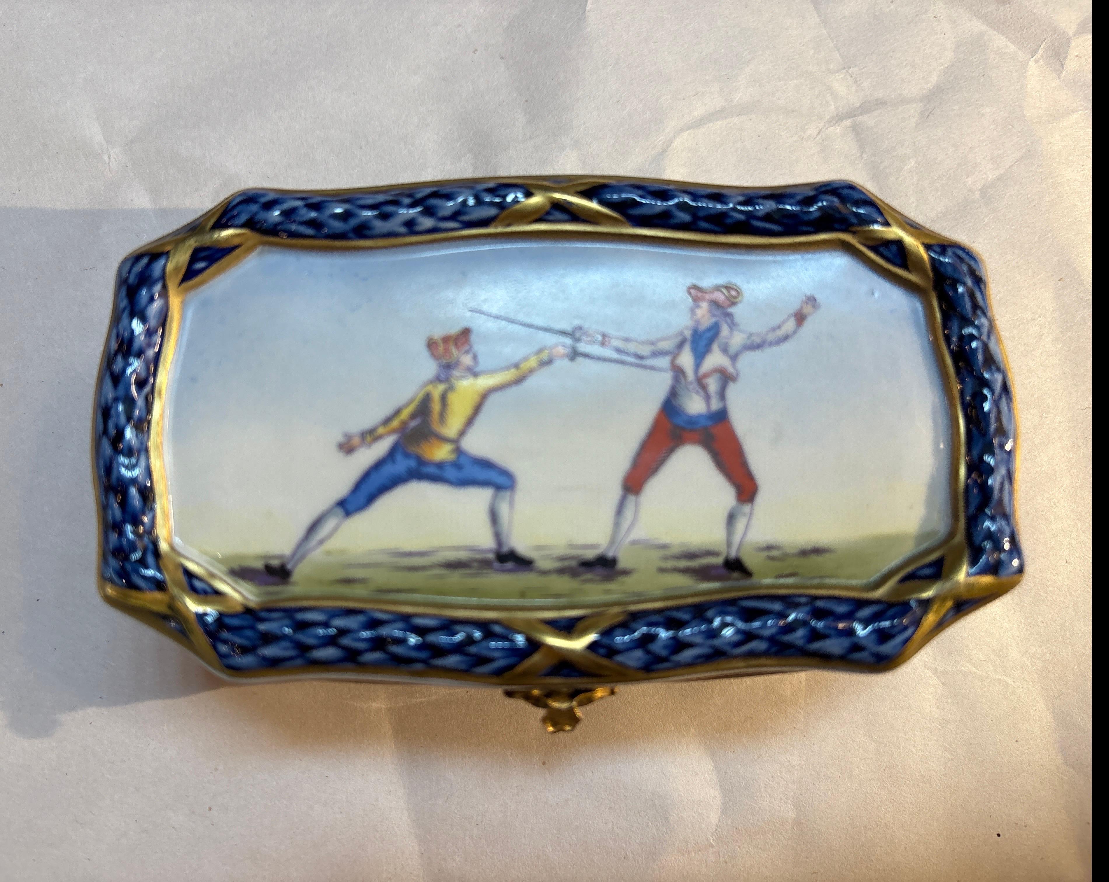 Kleine Dose aus französischem Sèvres-Porzellan, handbemalt, mit Scharnierdeckel.  Die lebendige Farbe mit vergoldeten Akzenten zeigt Fechter im Stil des 18. Jahrhunderts mit einem kobaltblauen Rand.  Markiert auf der Unterseite, 5 Zoll lang. 