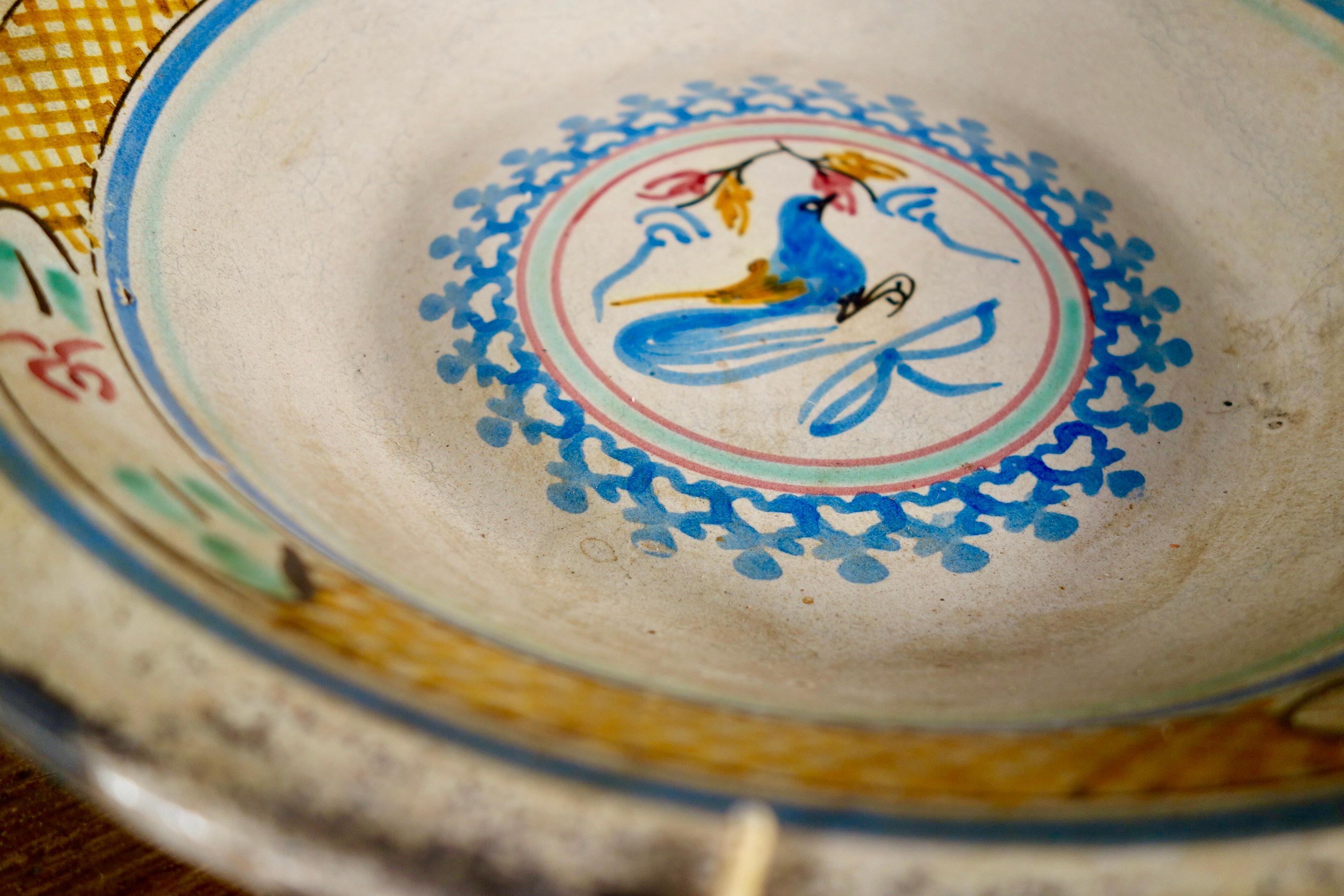 A Spanish tin glaze bowl, featuring vivid repetitive geometric style decorations, with the center base of the bowl featuring a blue hand painted bird. Displaying simplistic designs throughout with strong tones of yellow pink and blue.
Measures: