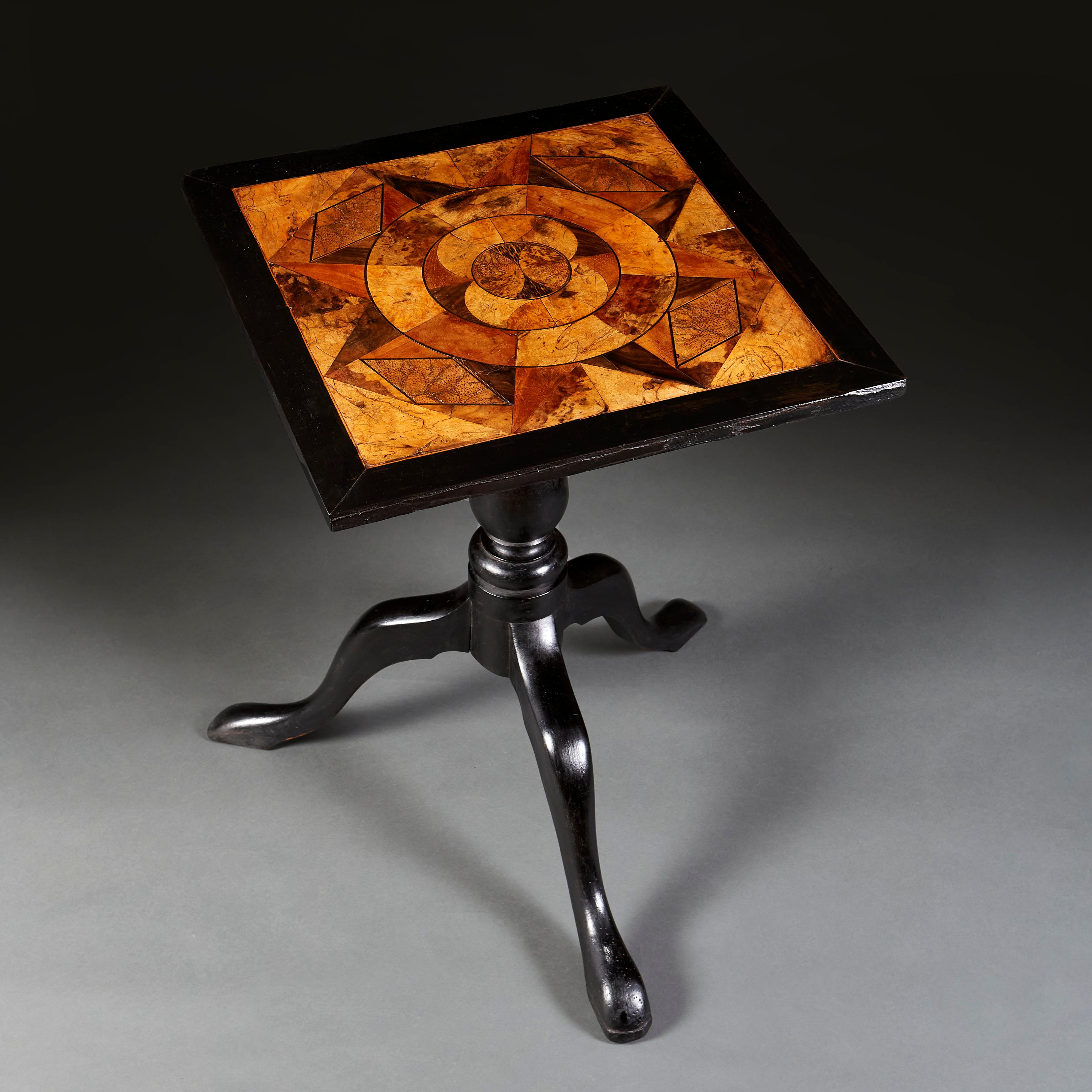 A mid nineteenth century ebonised occasional table with top incorporating rare and exotic specimen woods, all supported on a tripod base.