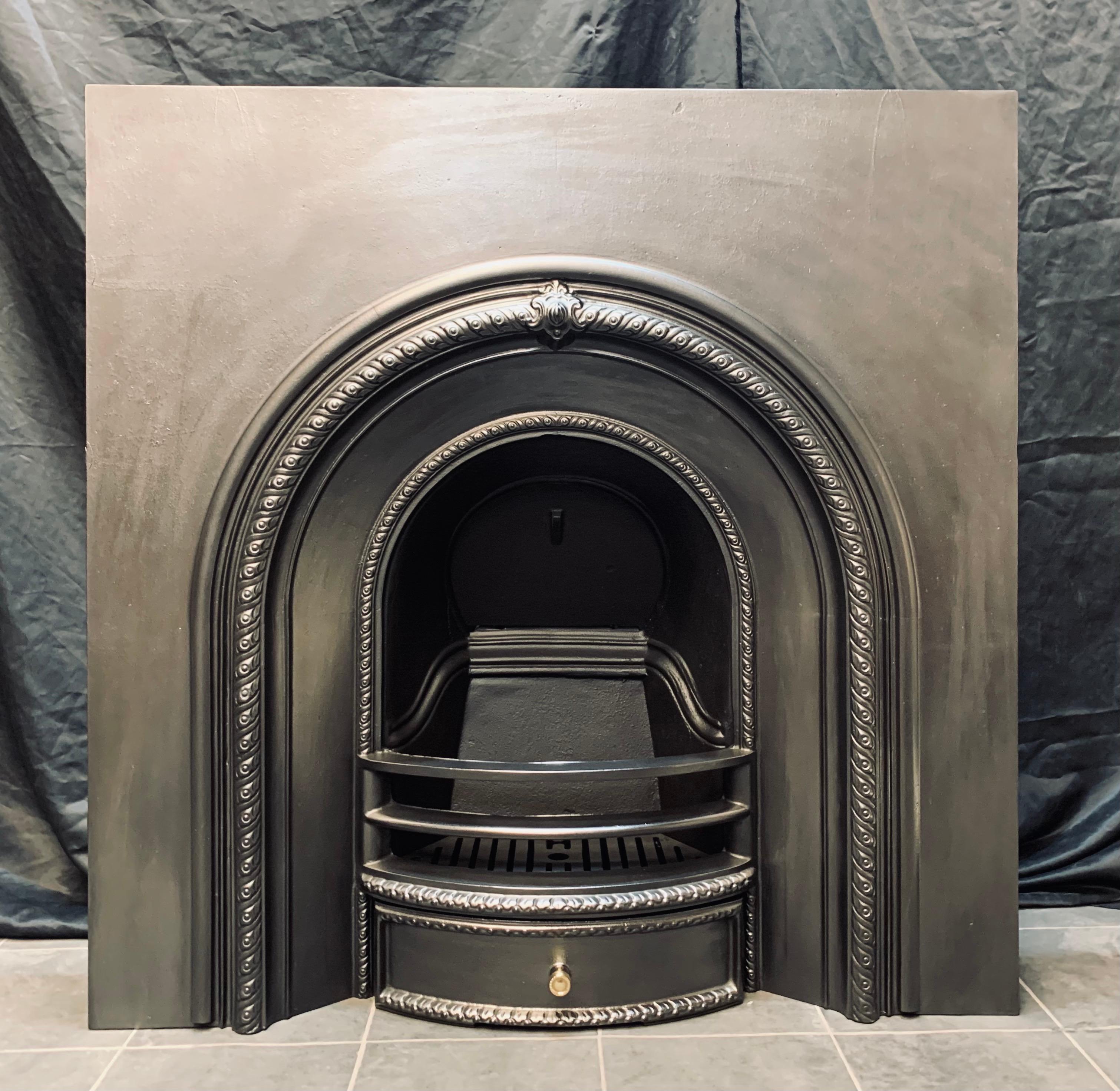 A simple and well cast 19th century style arched fireplace insert. A raised rope border with a central cartouche, a three barred curved fire front and ash pan door, complete with its original ash pan and grate. 

English.