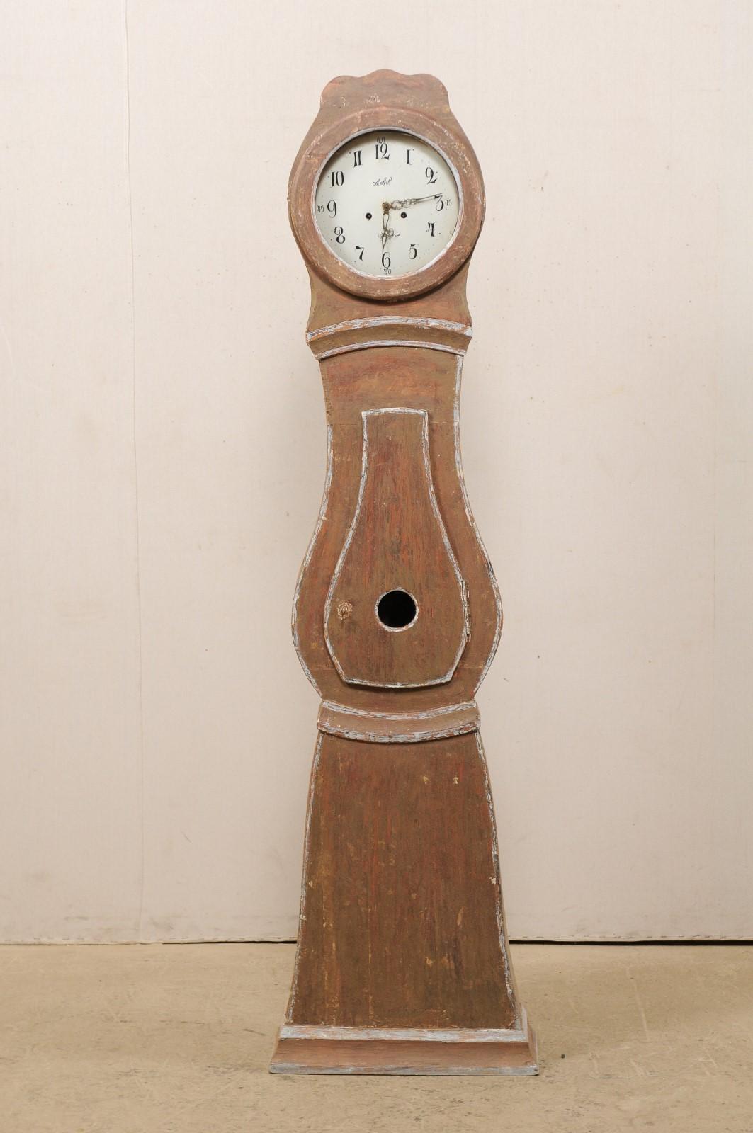 A Swedish painted wood mora clock from the 19th century. This antique mora clock from Sweden features a subtle scalloped crown adorning it's head, a teardrop-shaped door and belly, triangular lower section, and is supported upon a flat platform