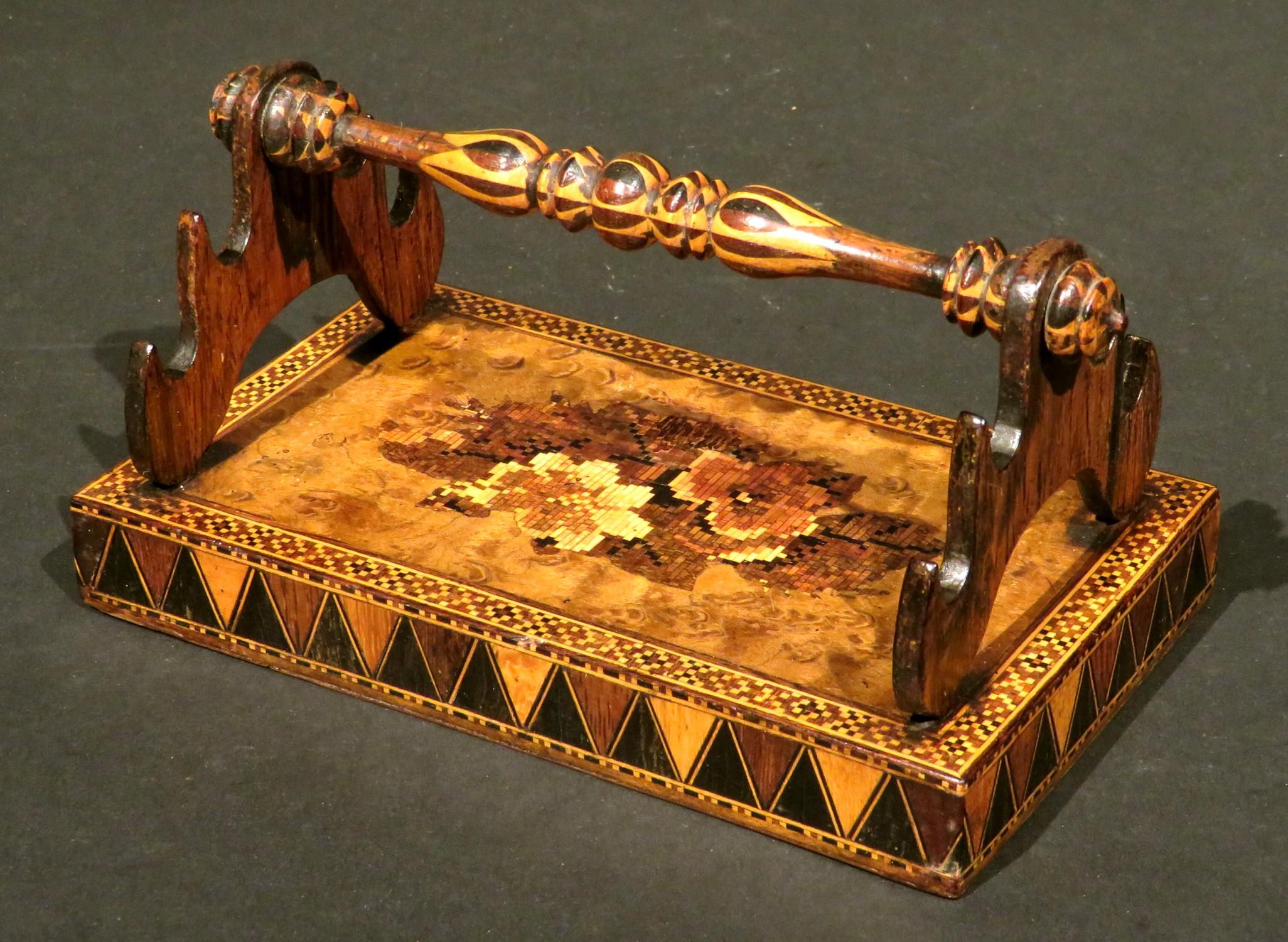 Showing a finely turned fruitwood-handle / pen-rest, affixed to a weighted burl wood base decorated with geometric and floral motifs in stick-work and tessellated mosaics, the sides decorated with geometric inlays of contrasting light and dark woods.