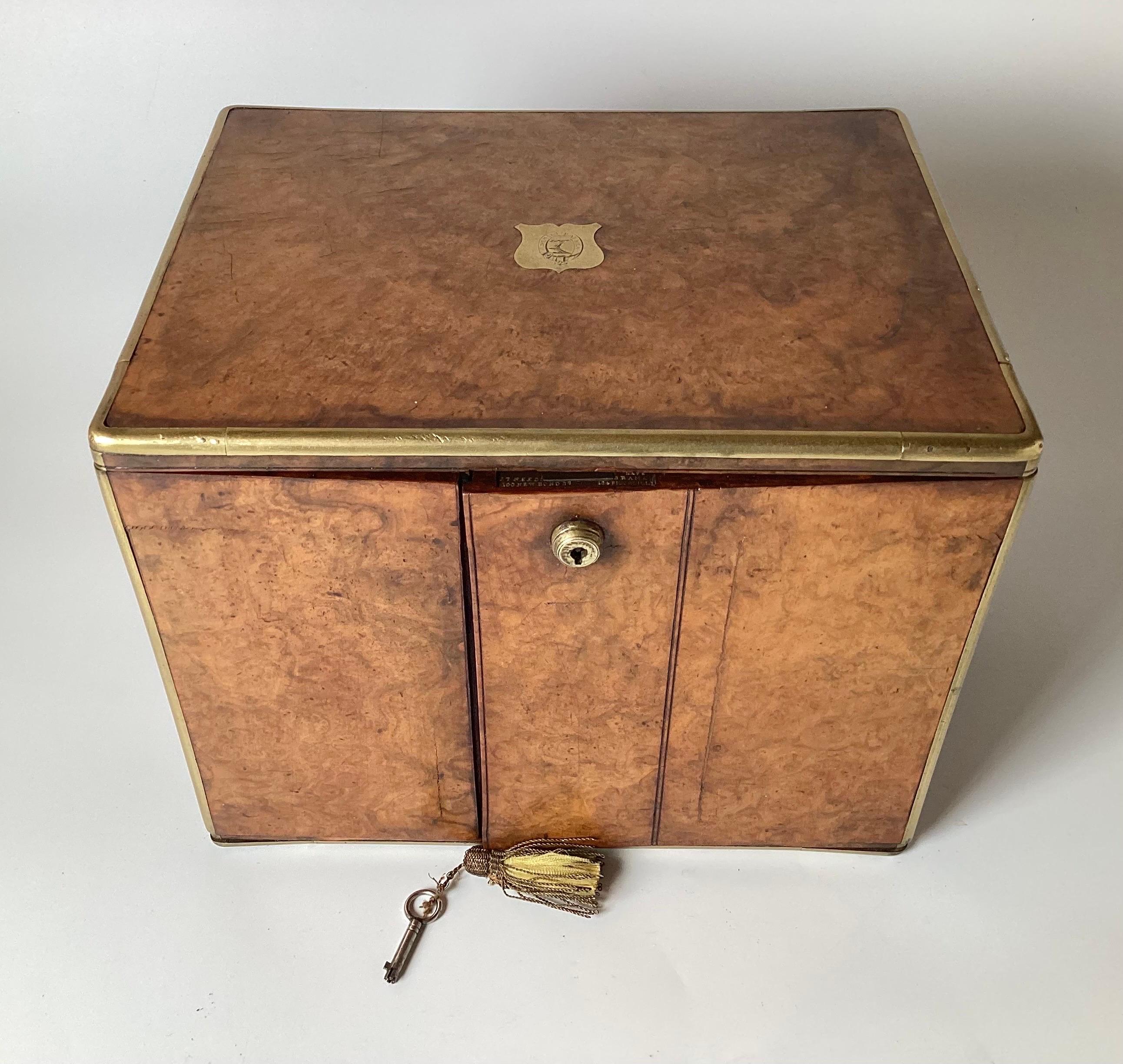 A diminutive table top campaign chest, cigar box. The walnut box with brass trim and handles with two doors that open to reveal two drawers with compartments. Working lock with key, with brass plaque engraved in Latin, translation 