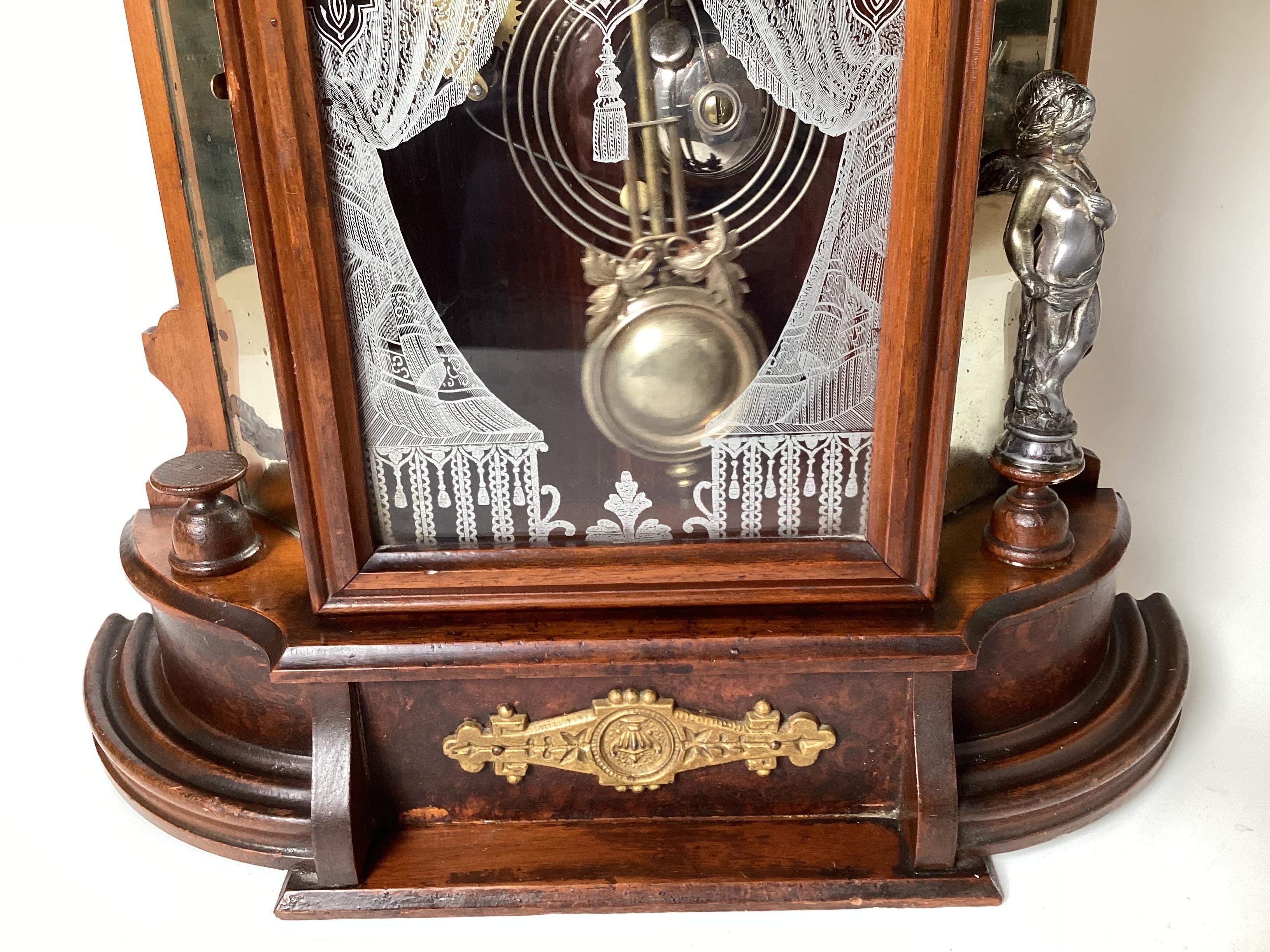 A carved walnut mantle clock made by William Gilbert, Connecticut, circa 1880.  The top with walnut fan pediment with mirrored side panels with a center glass door with white drape form decoration.  The clock that strikes on the hour and half hour,